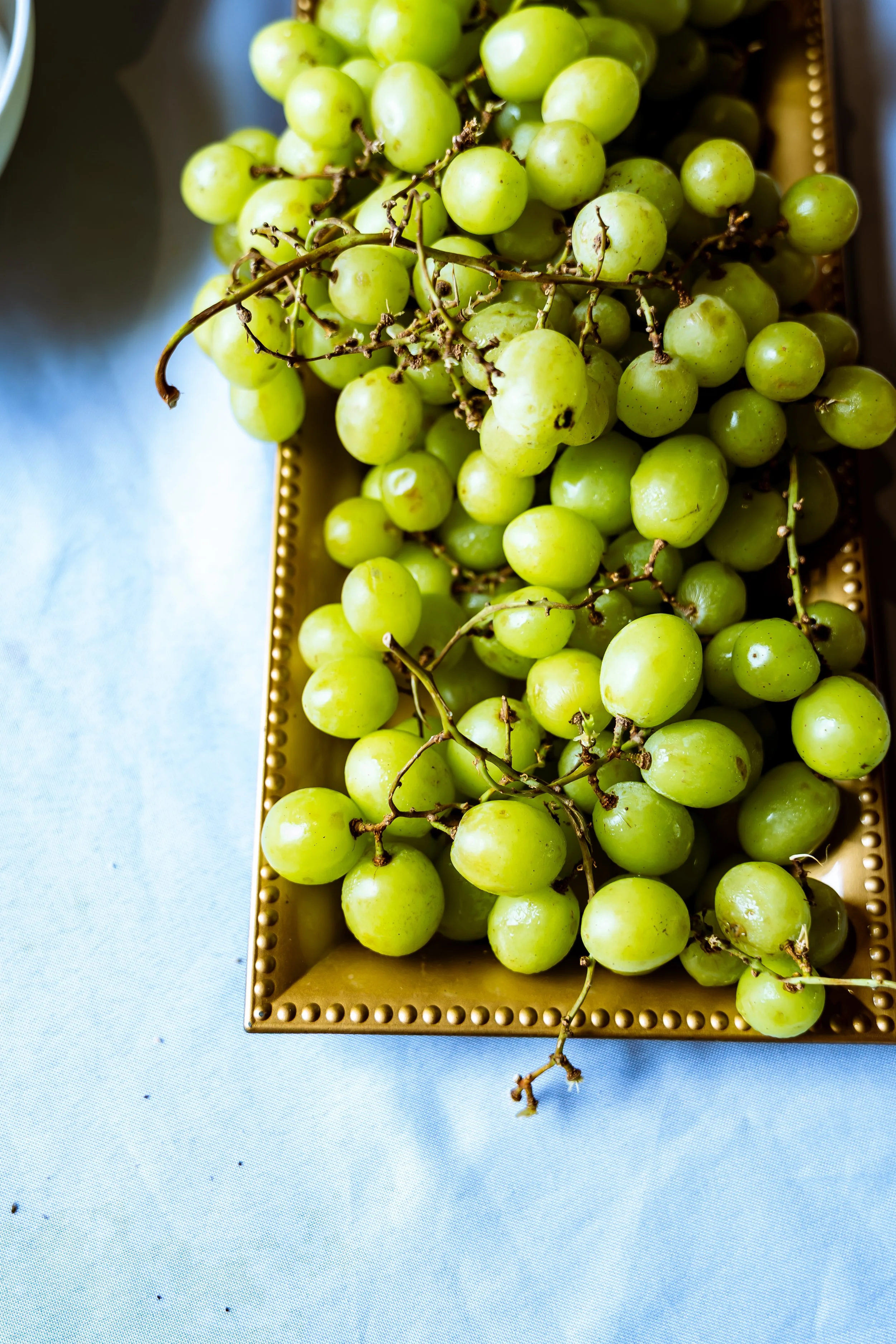 Green grapes on a golden tray placed on a light blue surface.