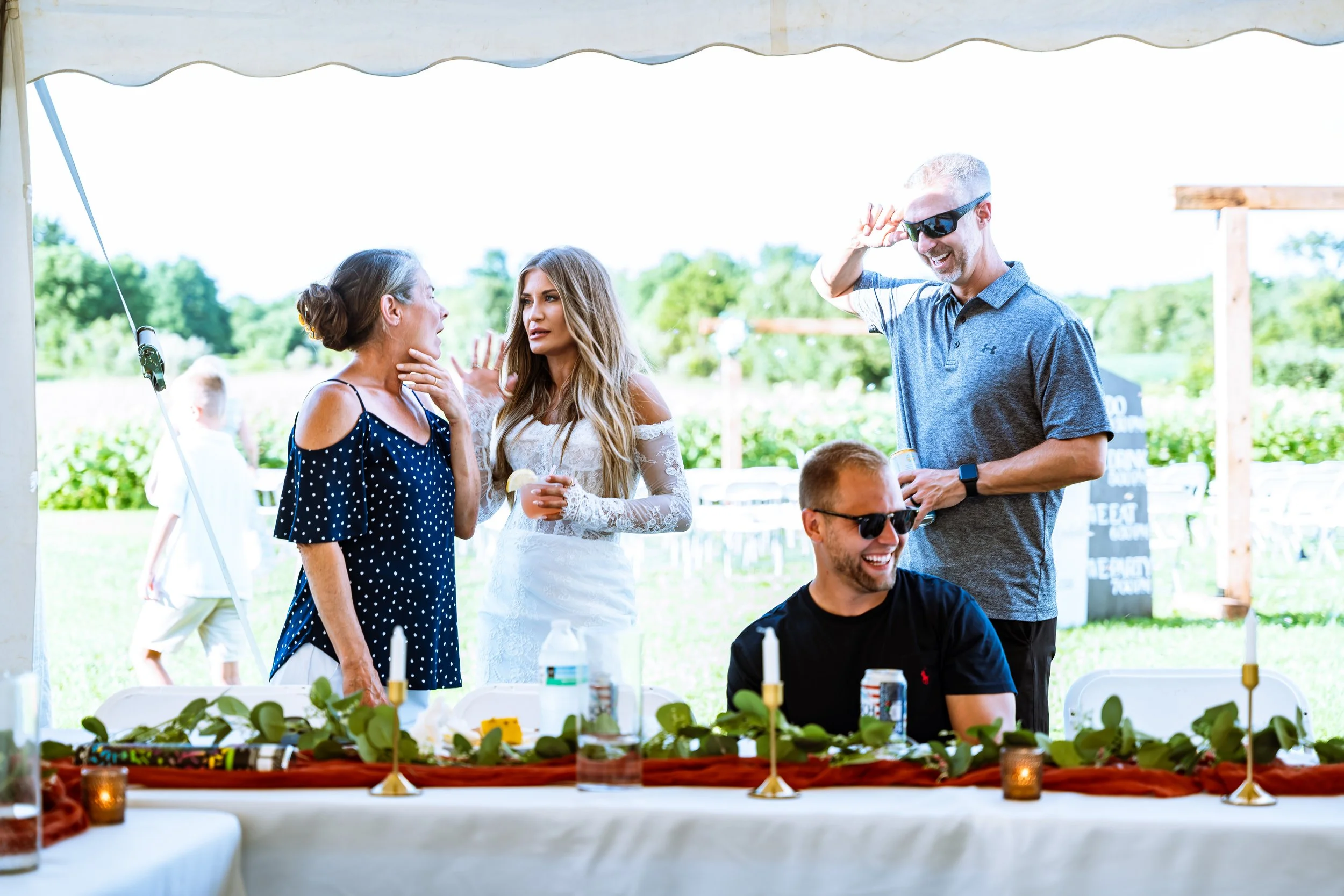 People socializing at an outdoor party under a tent with a decorated table in the foreground.