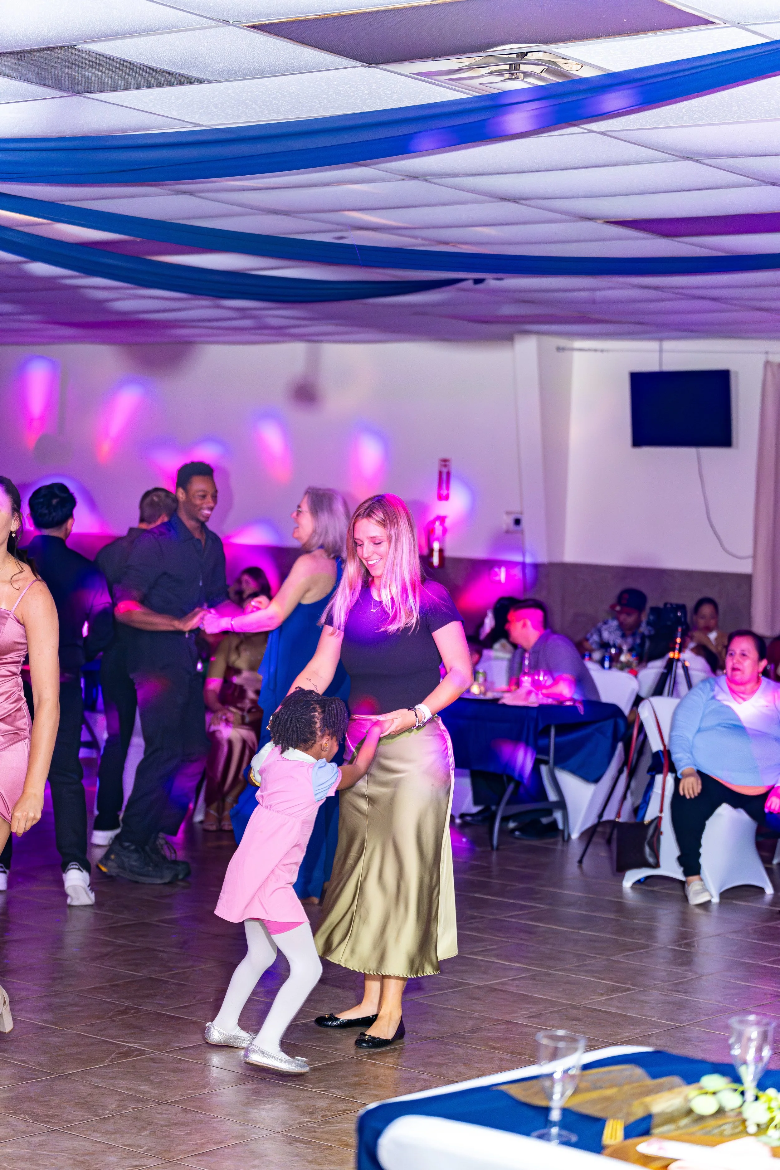 People dancing at an indoor party or celebration with colorful lighting and decorations.