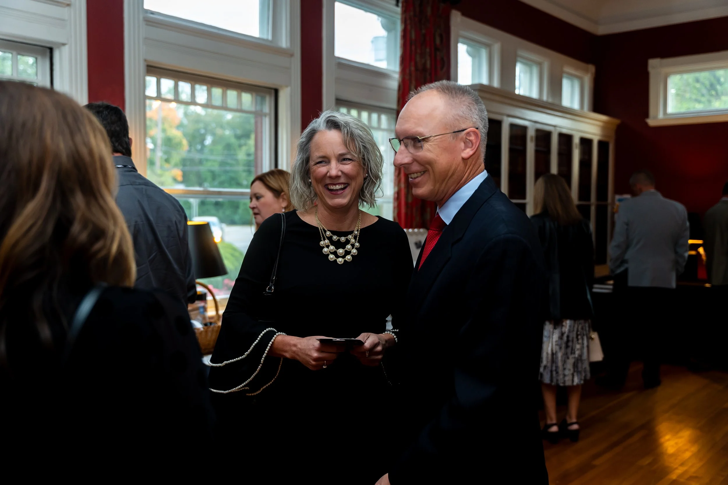 A group of people at a social gathering indoors, with a man and woman in conversation smiling, while others are in the background.