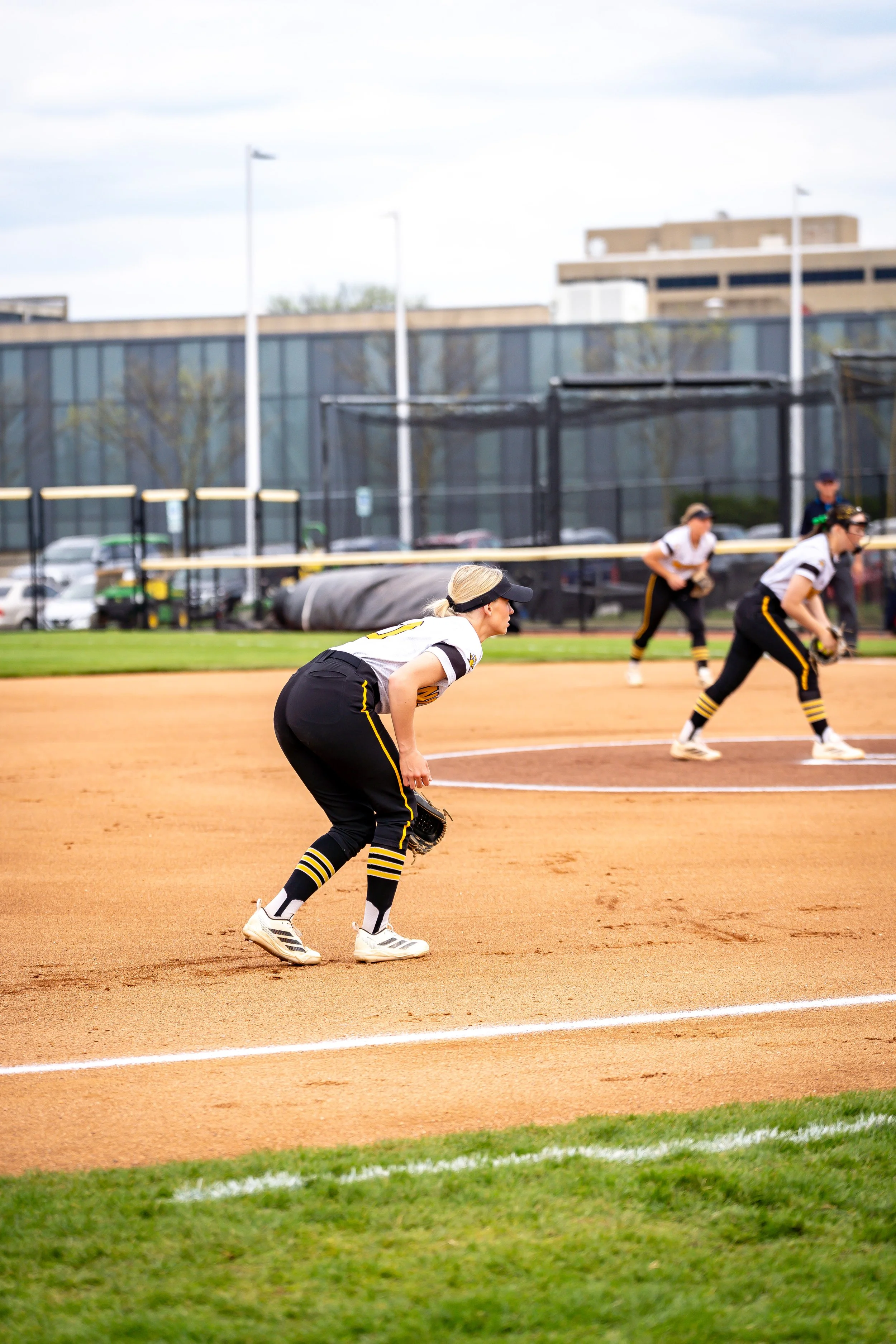Women softball players on the field during a game, with a woman in the foreground preparing to catch the ball.