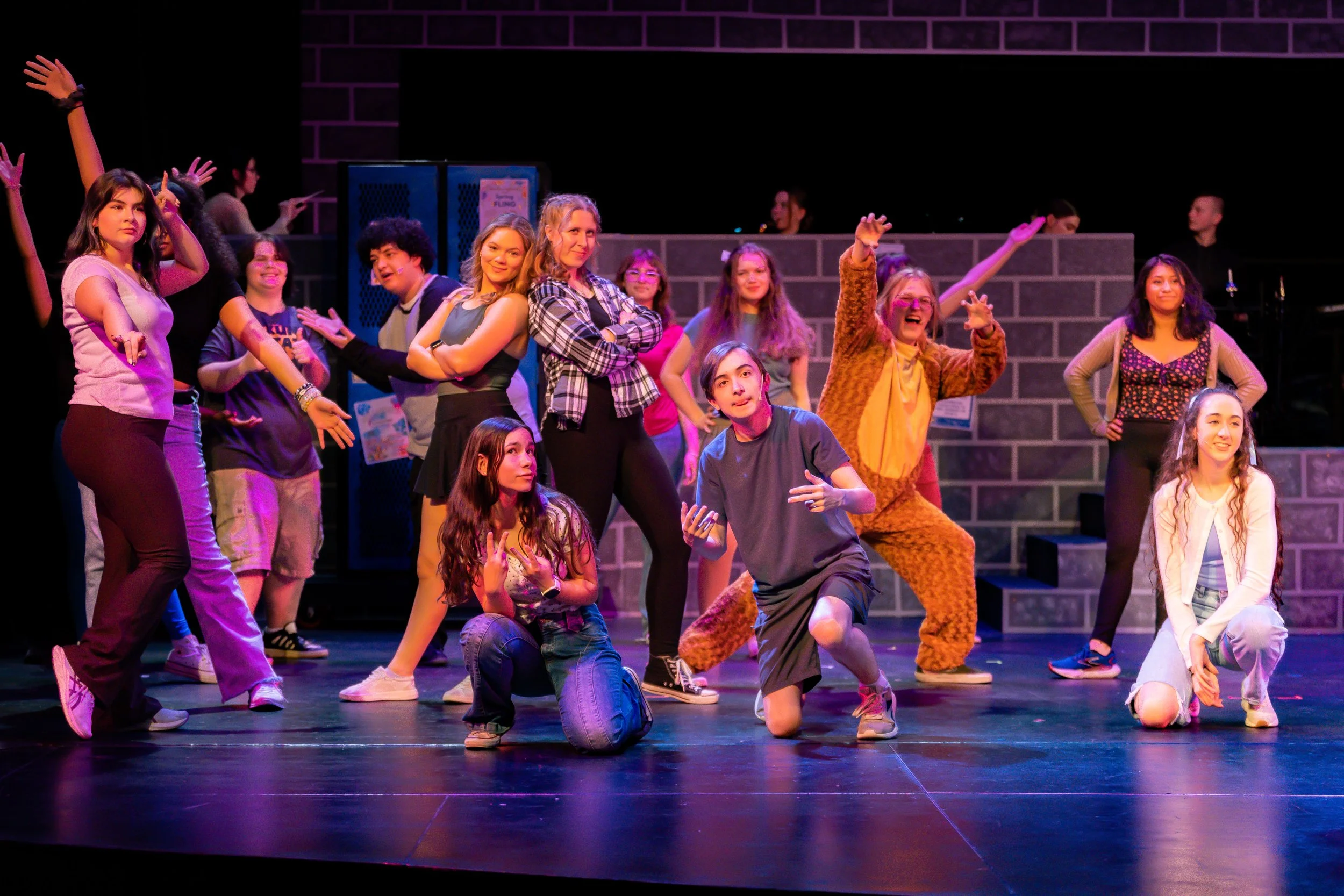 A group of young people performing a dance on a stage, with cityscape props and colorful lighting.