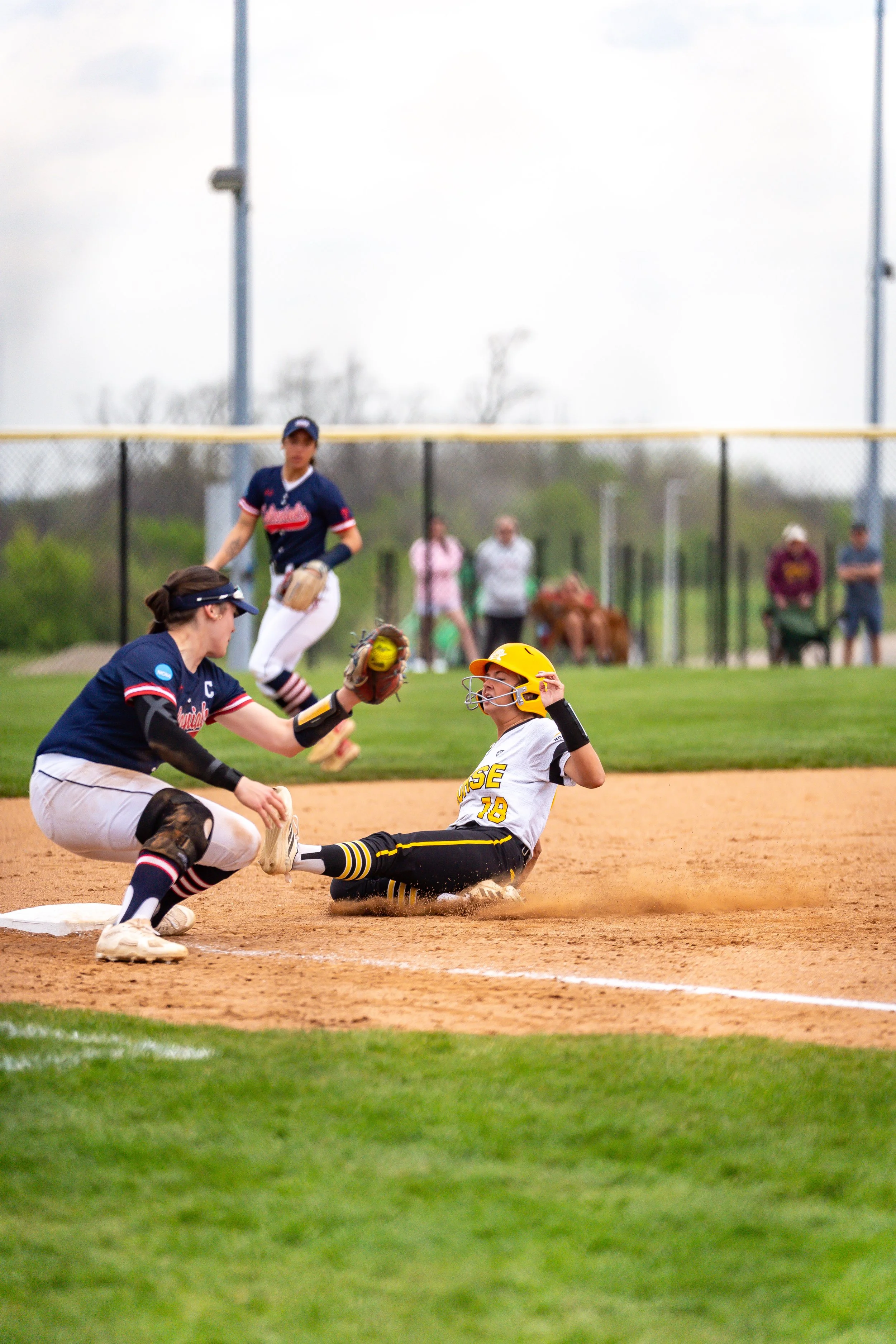 A baseball game in progress with players in action on the field, focusing on a slide into a base with spectators watching.