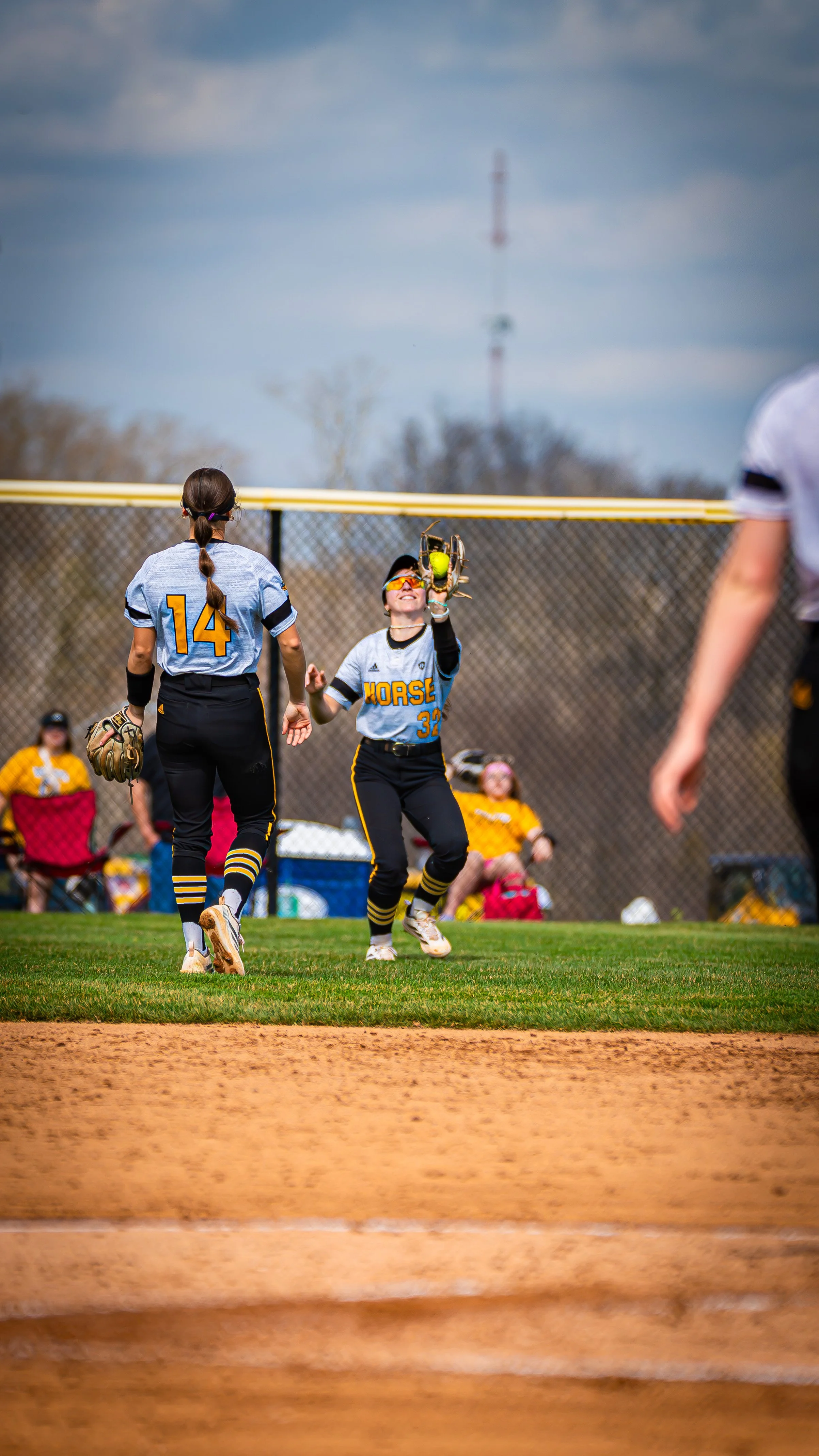 A softball game in progress with players wearing blue and yellow uniforms, one girl catching a ball, and others on the field.