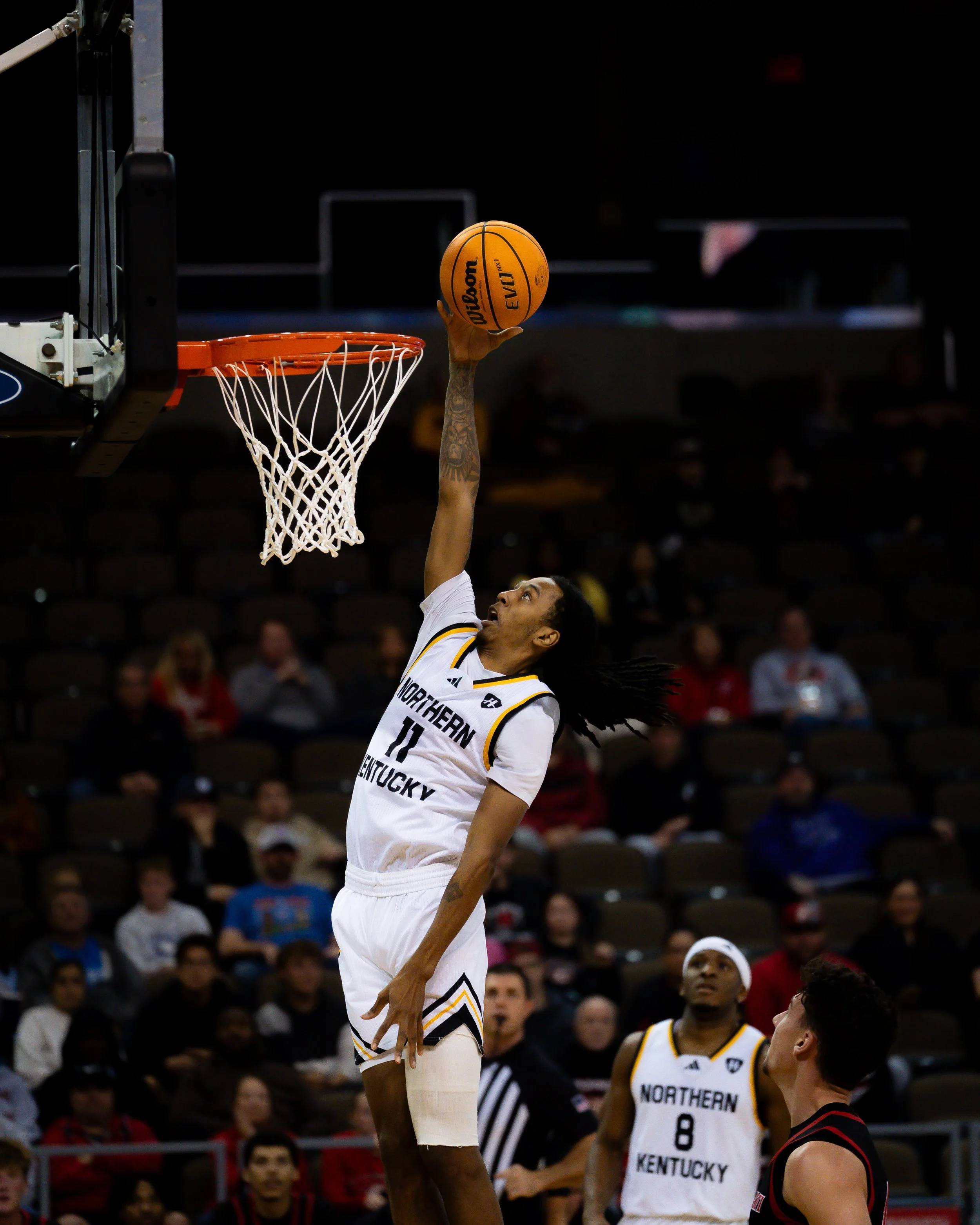 A basketball player from Northern Kentucky leaping to make a shot during a game, with an audience in the background.