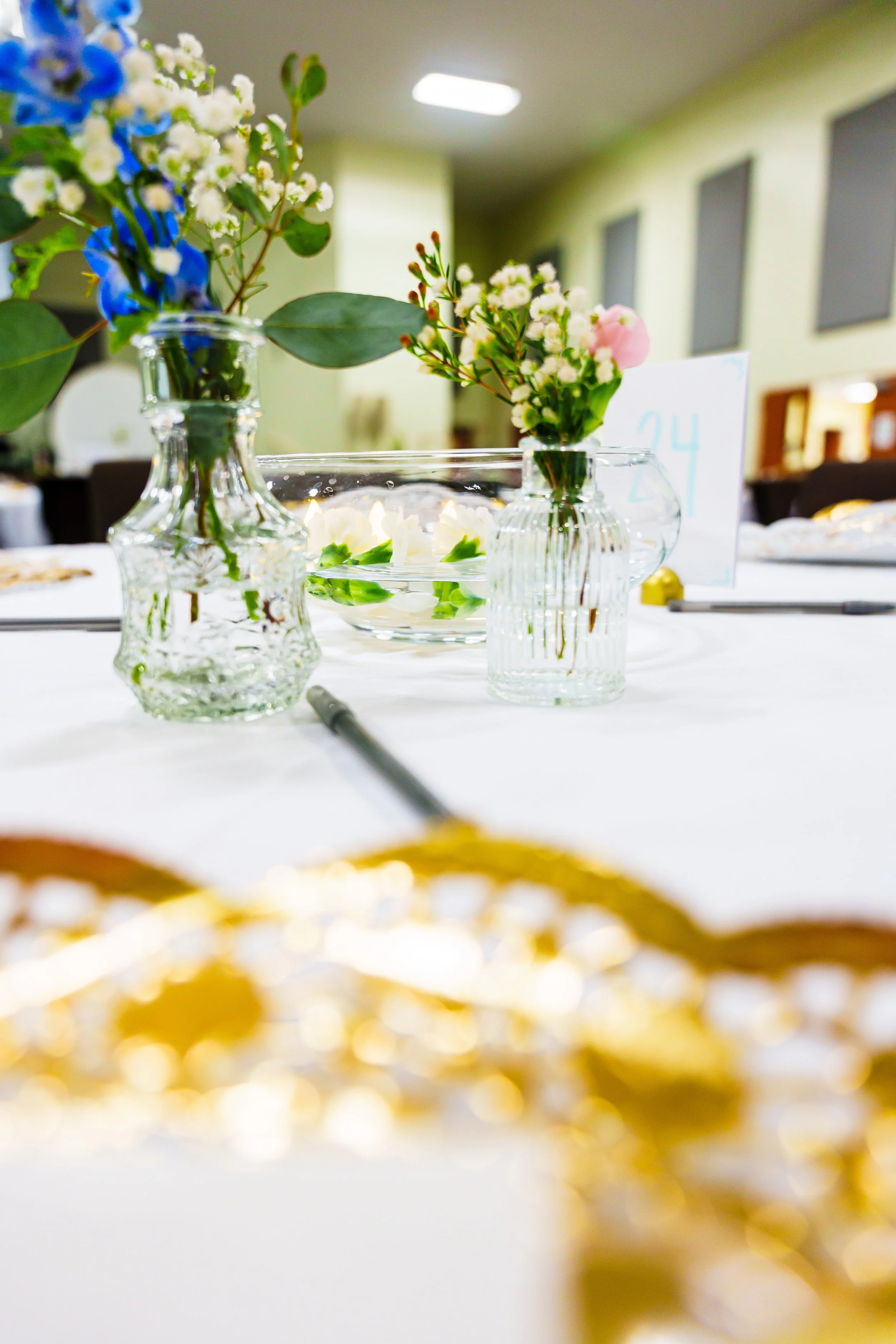 Close-up of a floral centerpiece with white, pink, and blue flowers in glass vases on a table at an event.