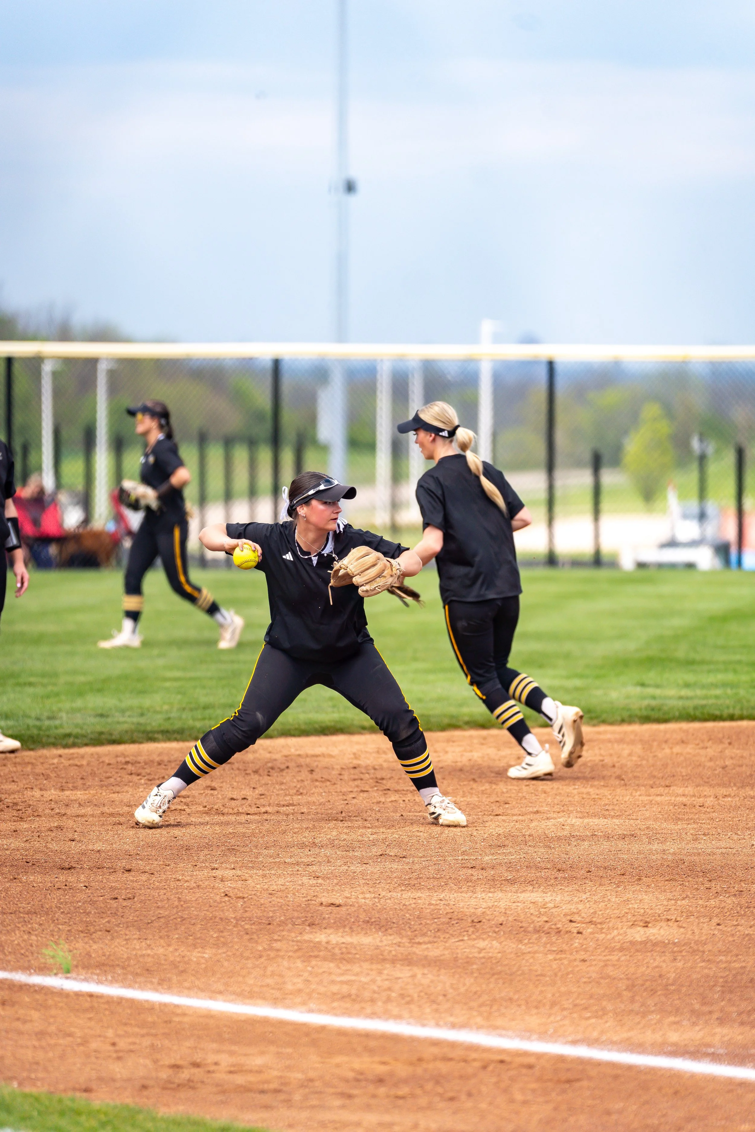 Women softbal players warming up on a field, wearing black uniforms and caps.