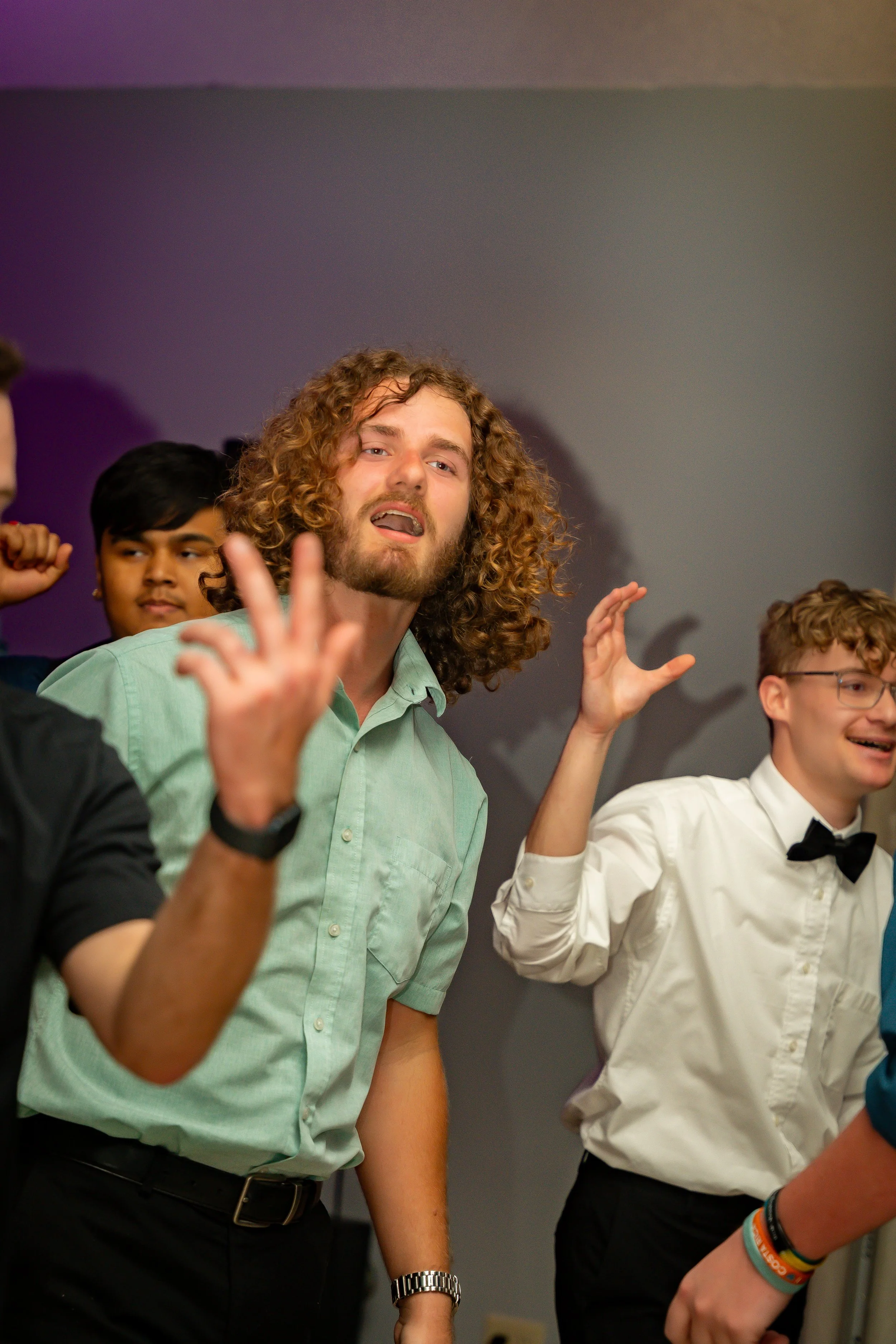 Group of young people at a social gathering, raising their hands and smiling.