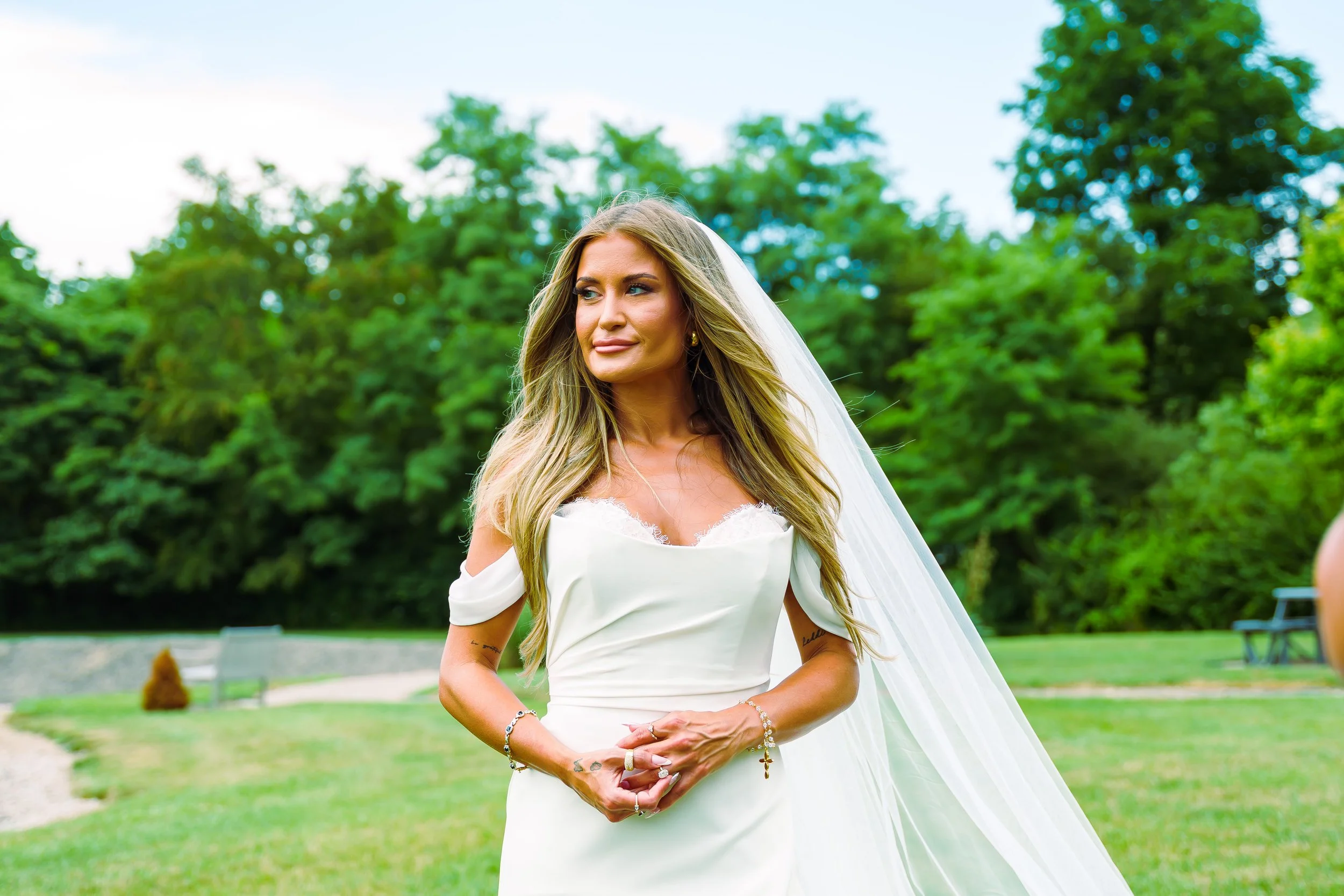 A woman in a wedding dress outdoors among trees and green foliage.