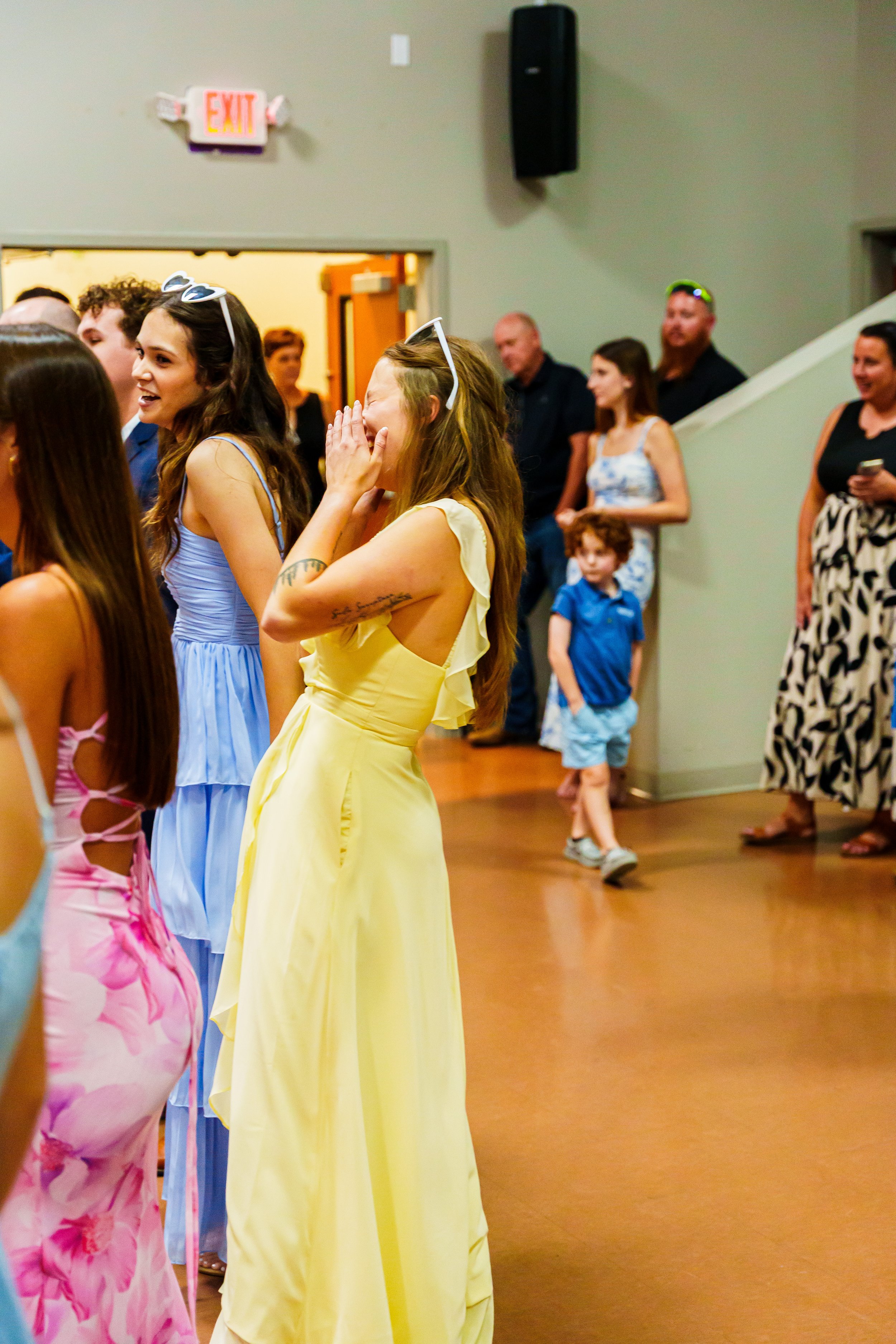 A group of people at a gathering, some laughing and smiling, with children in the background, indoors around a decorated event space.
