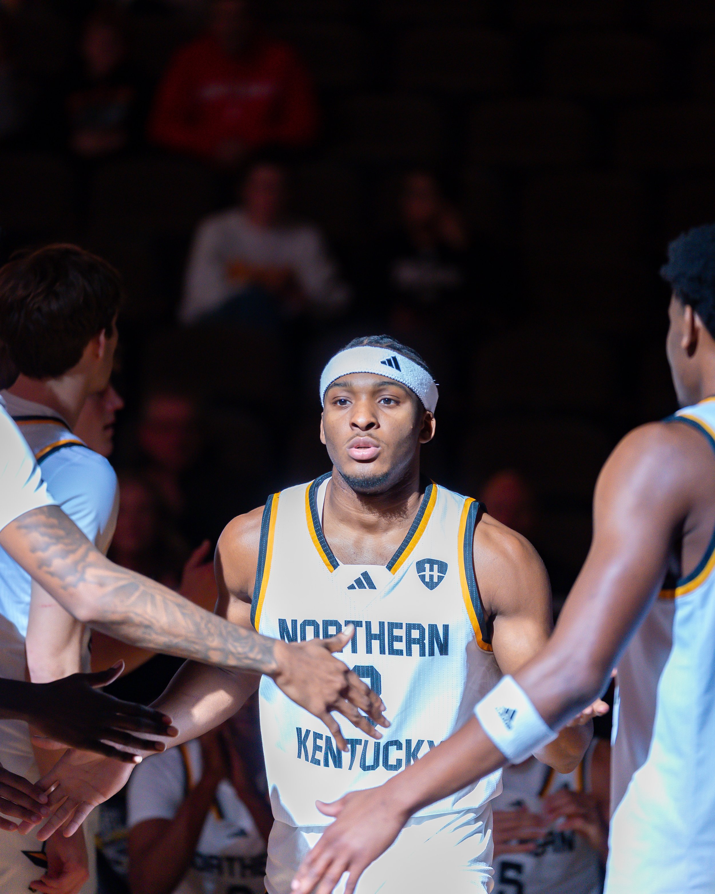 A basketball player wearing a white headband and jersey with 'Northern Kentucky' on it, engaged in a game or practice, surrounded by team members.