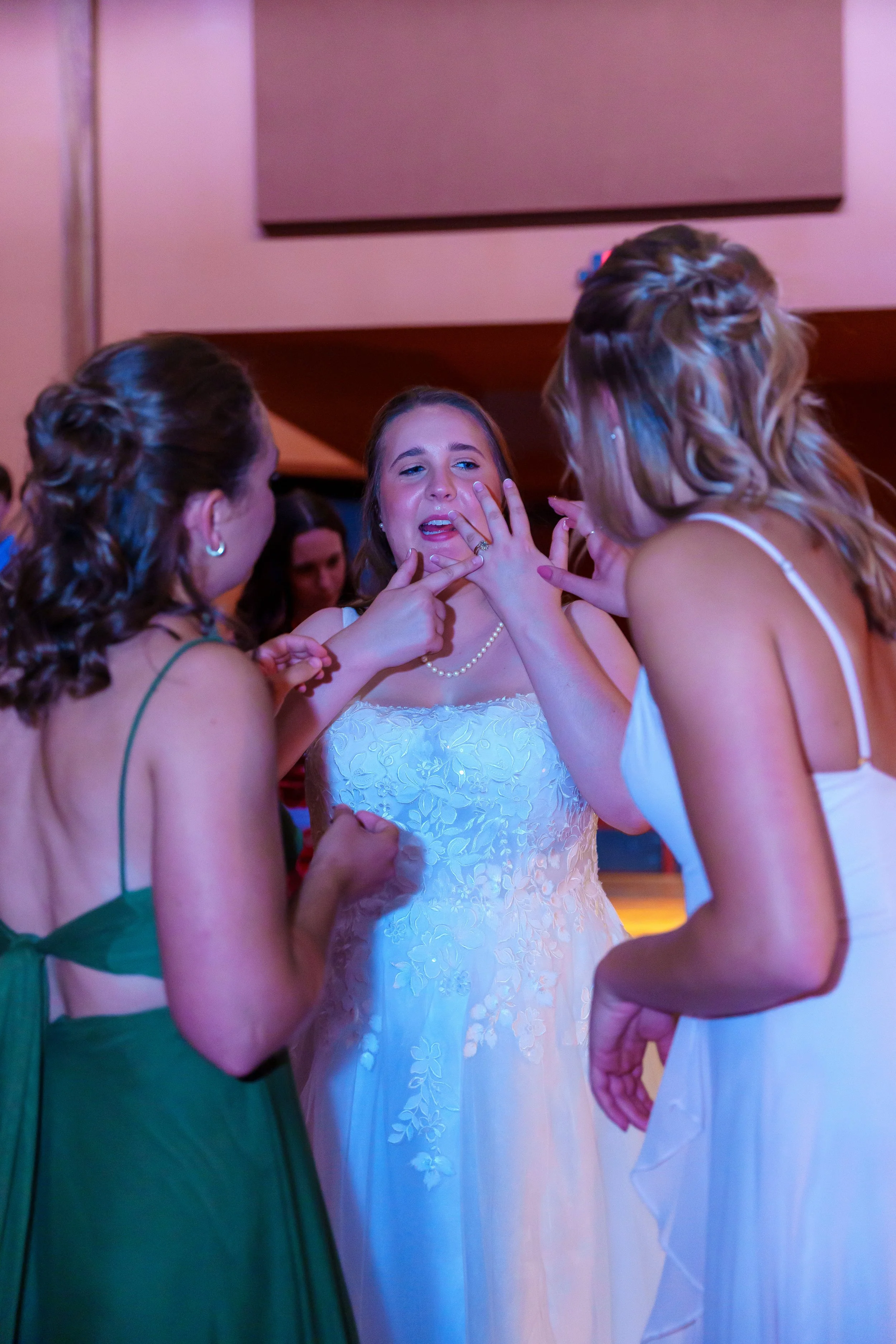 A bride in a white dress receives a touching moment with her bridesmaids at her wedding celebration.