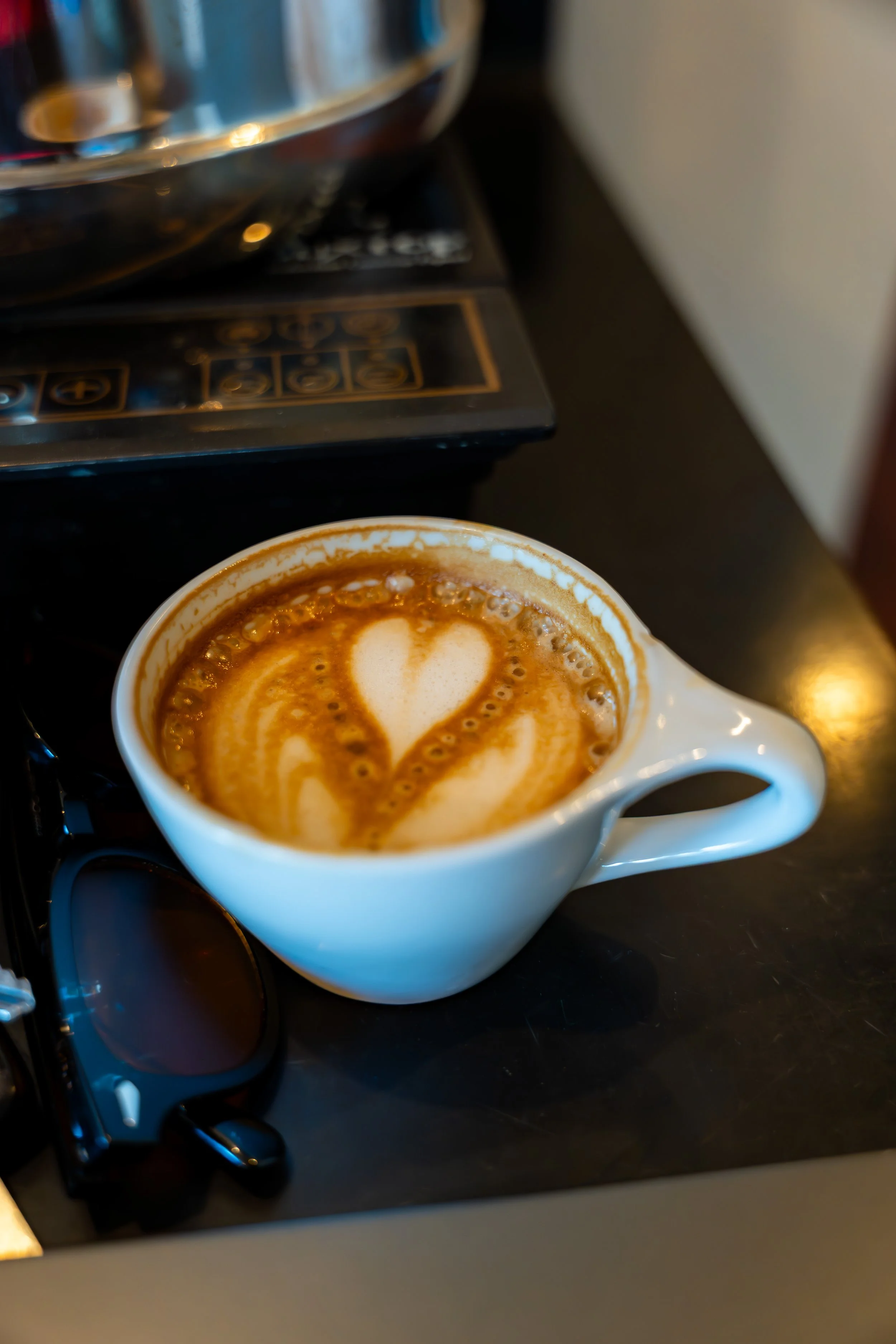 A white ceramic mug filled with a coffee beverage topped with latte art in the shape of a heart.
