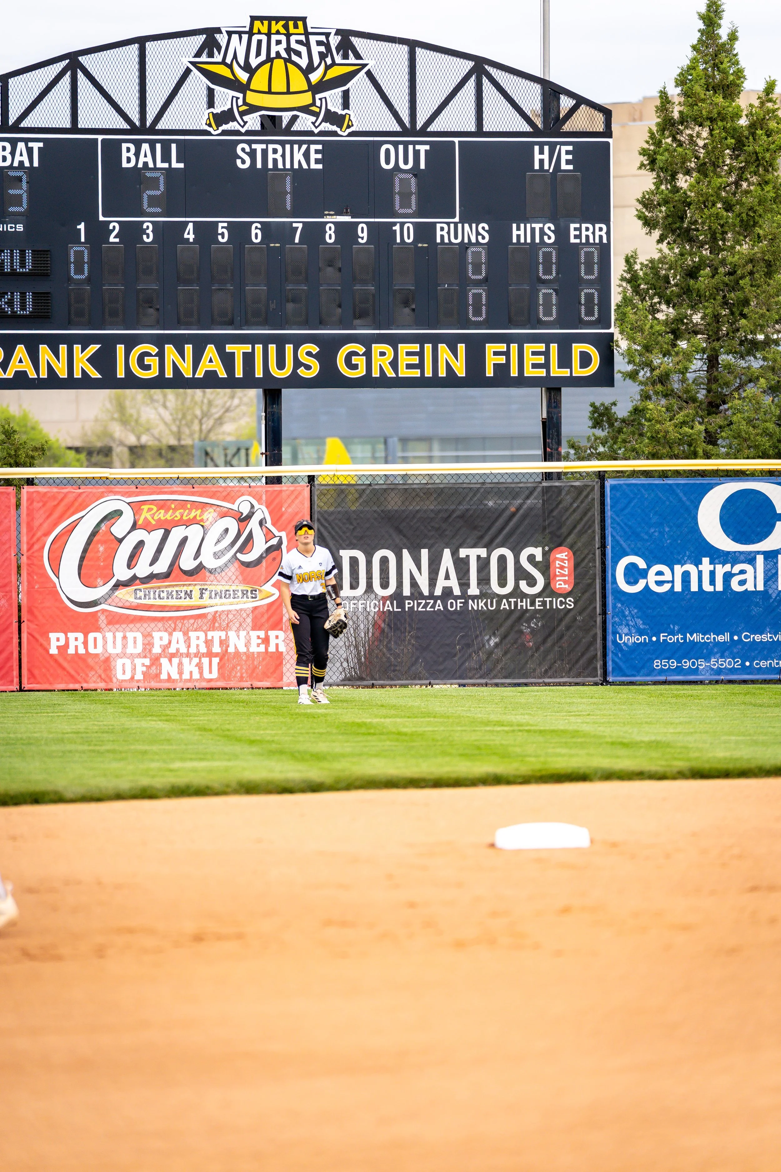 Baseball field with scoreboard, player, and advertisements in the background.