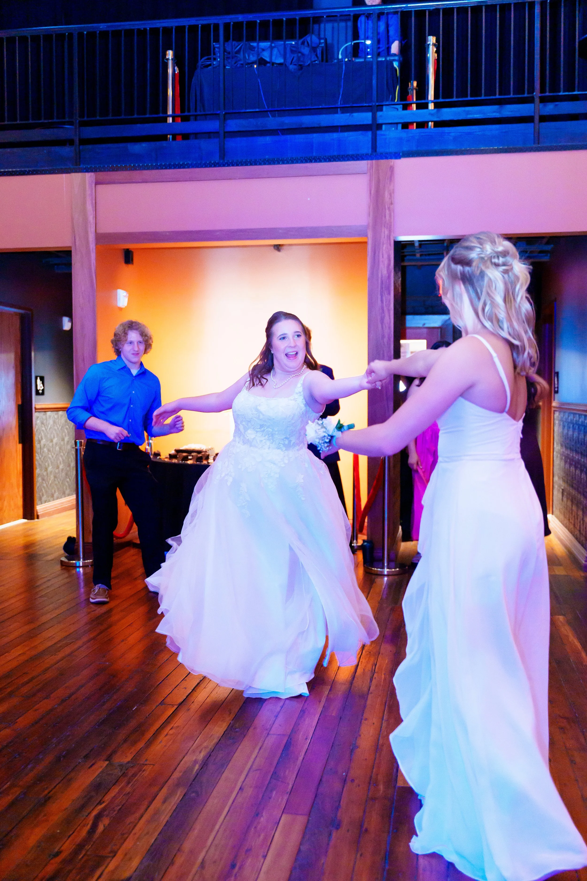 A bride dancing at her wedding reception with a woman in a white dress, on a wooden dance floor with colorful lighting.