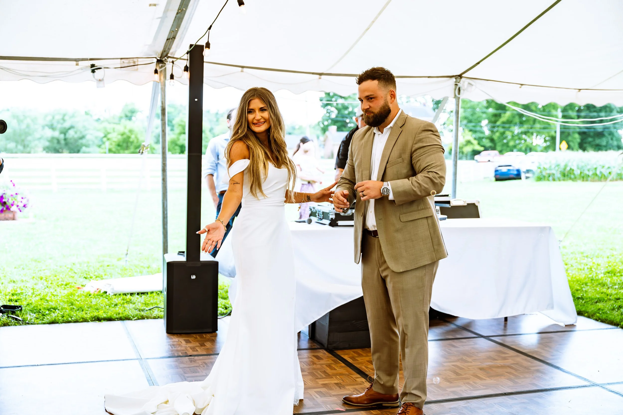 A bride and groom dancing at their outdoor wedding reception under a white canopy.