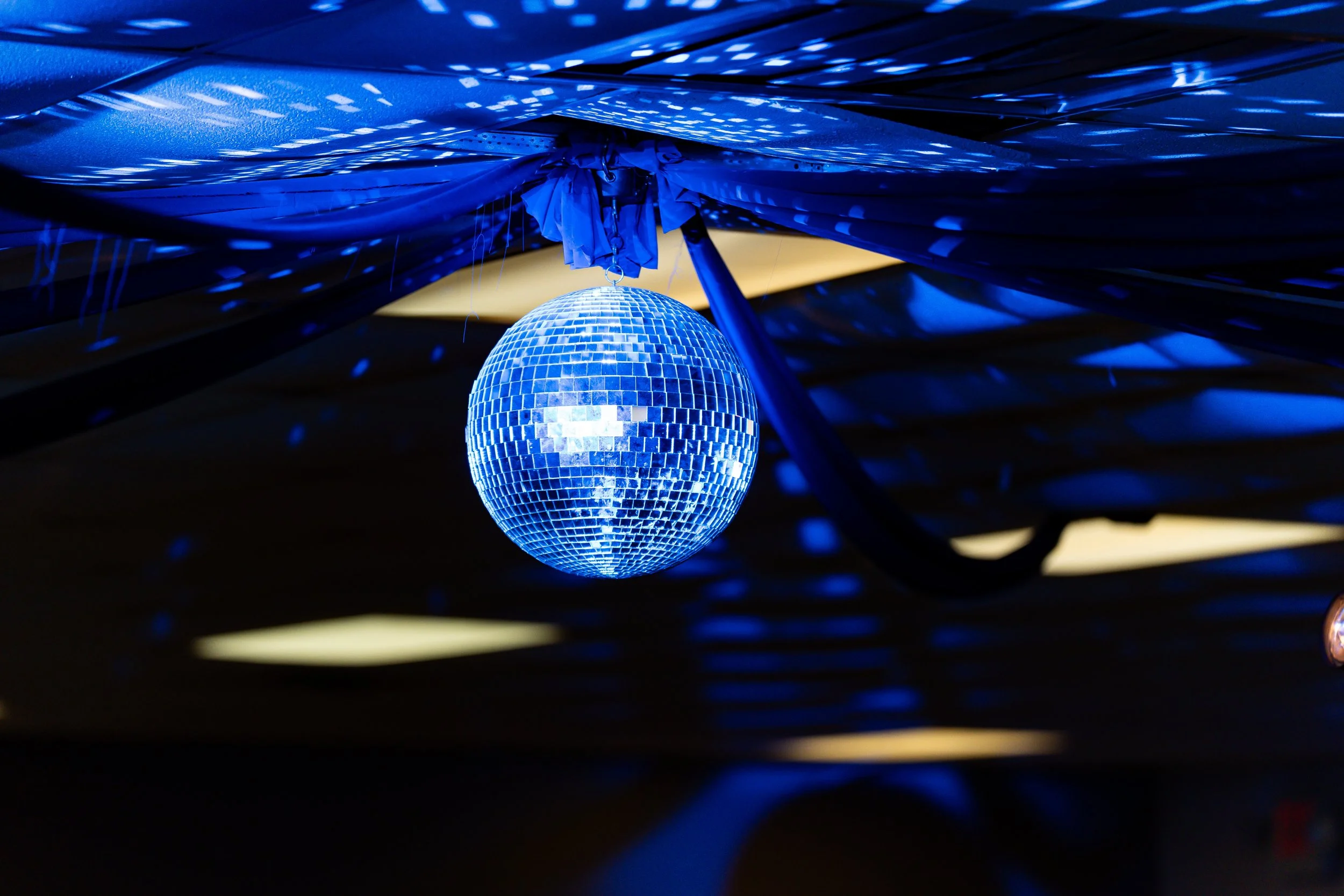 A disco ball hanging from the ceiling reflecting blue light patterns in a dark room.