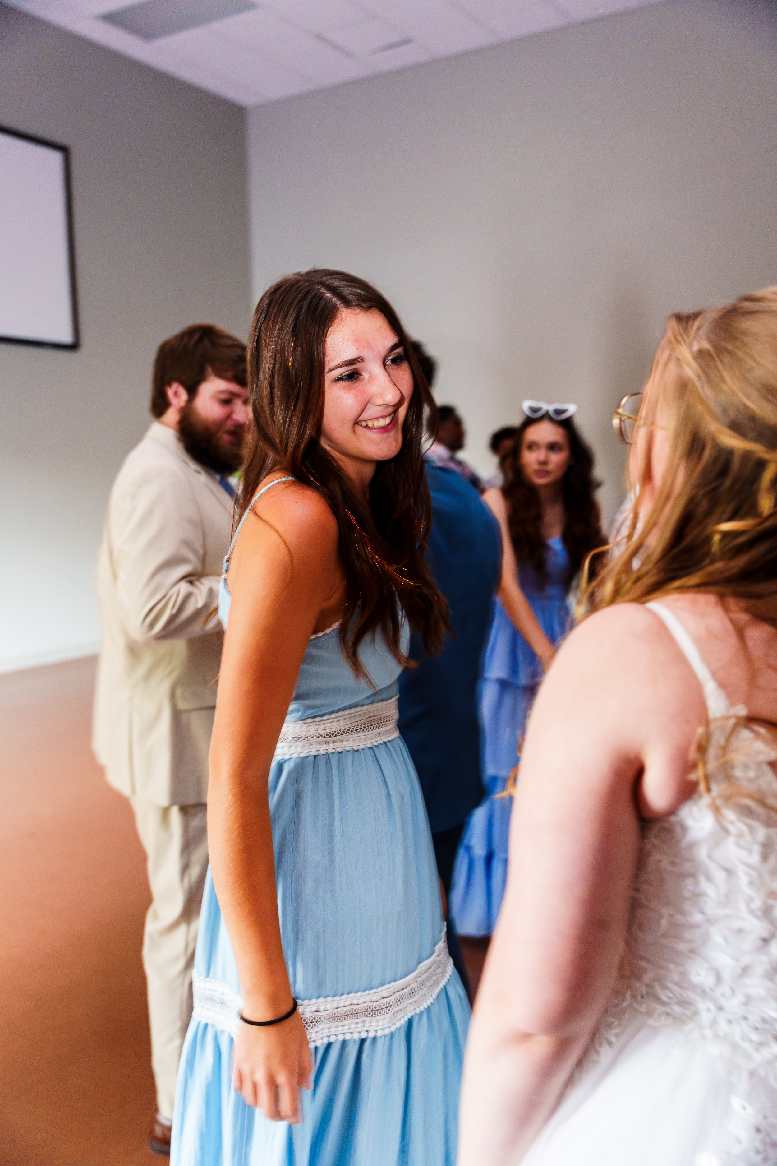 Group of young people at a social gathering, engaging in conversation and smiling, in an indoor setting with plain walls.