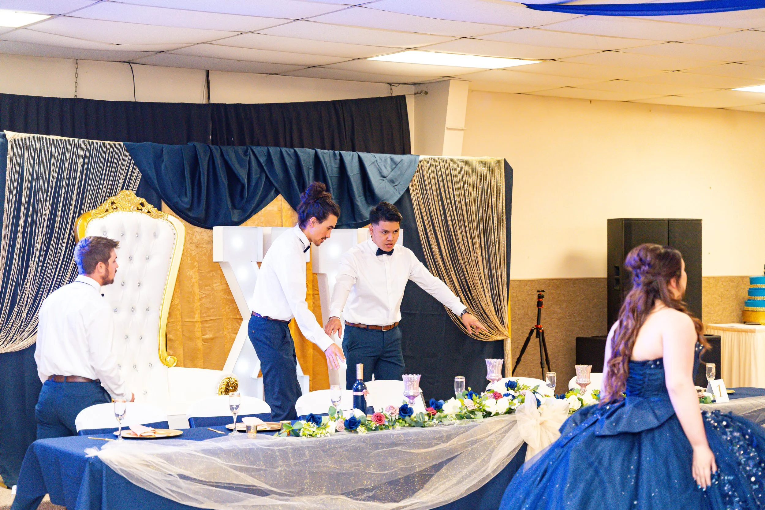 A group of young men dressed in white shirts and black bow ties preparing for a performance on a decorated stage at a formal event or celebration.