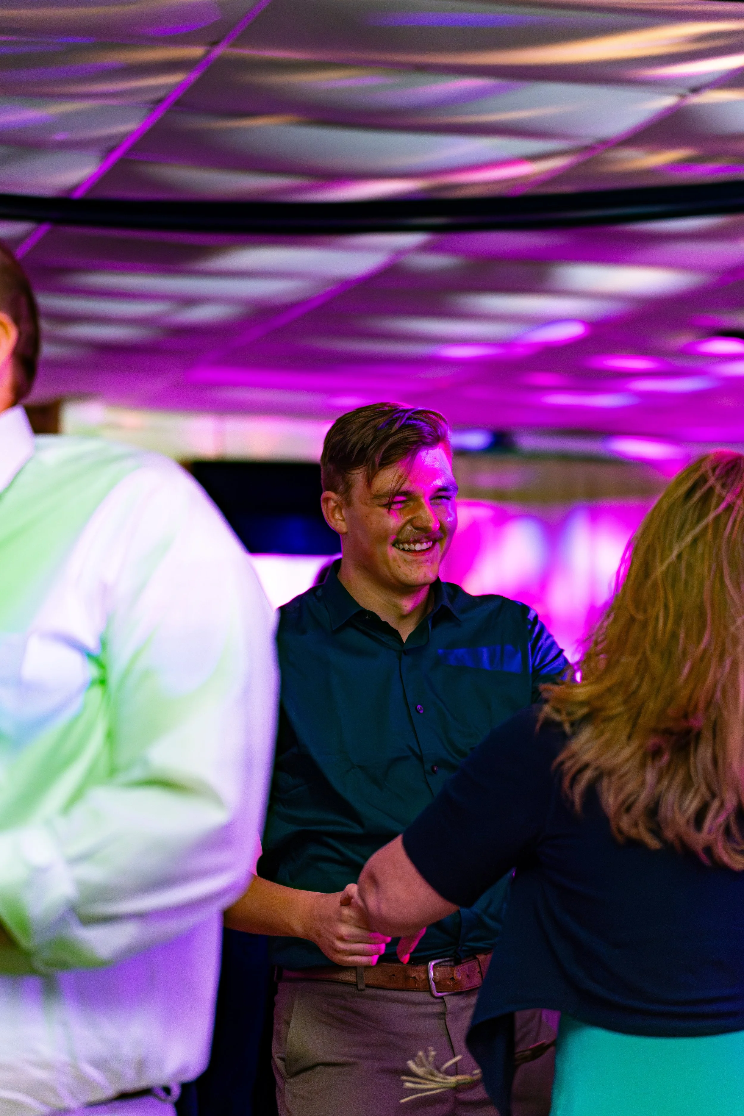 People at a social event shaking hands and smiling under colorful, purple and pink lighting.