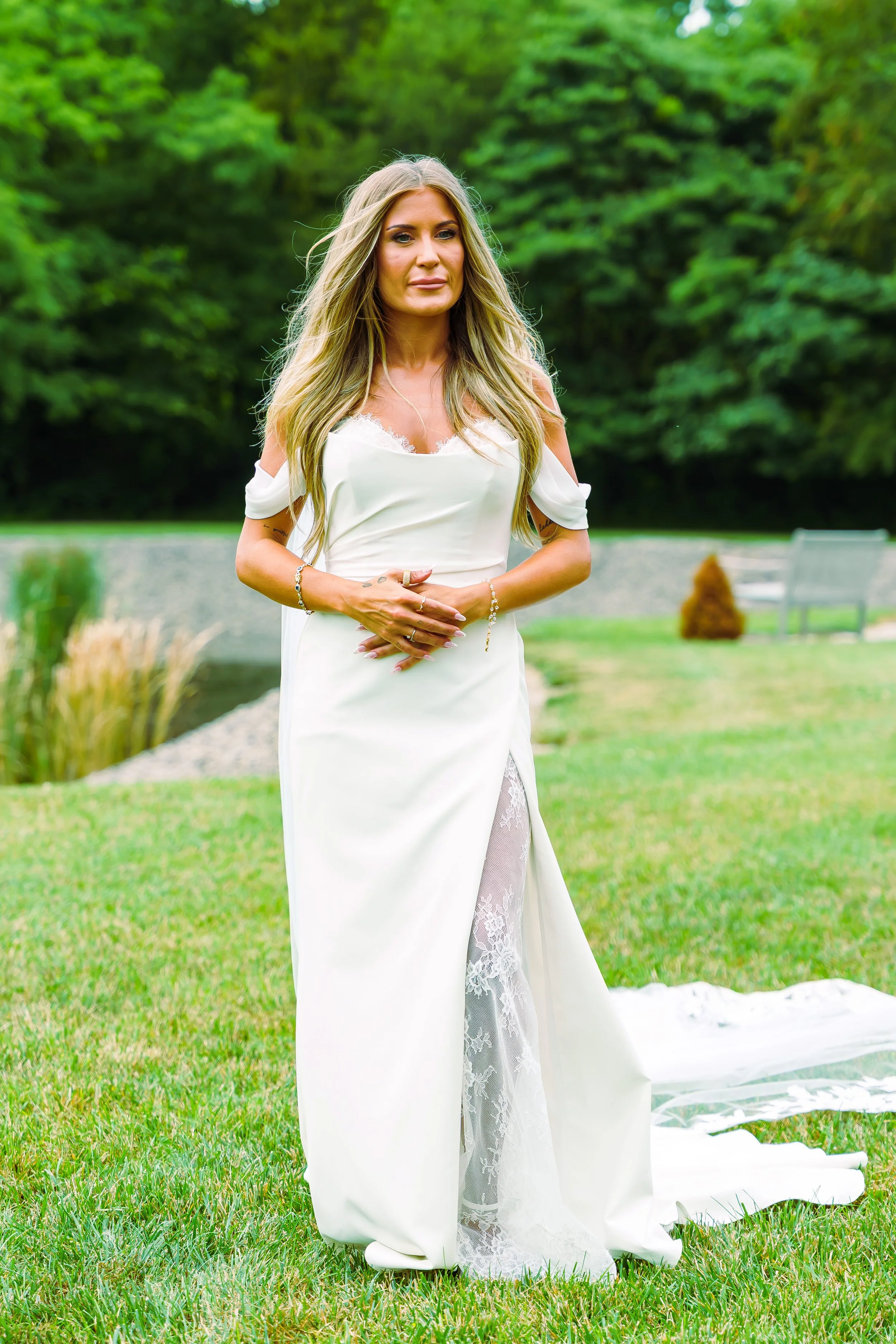 A woman in a white dress standing outdoors on grass with trees in the background.