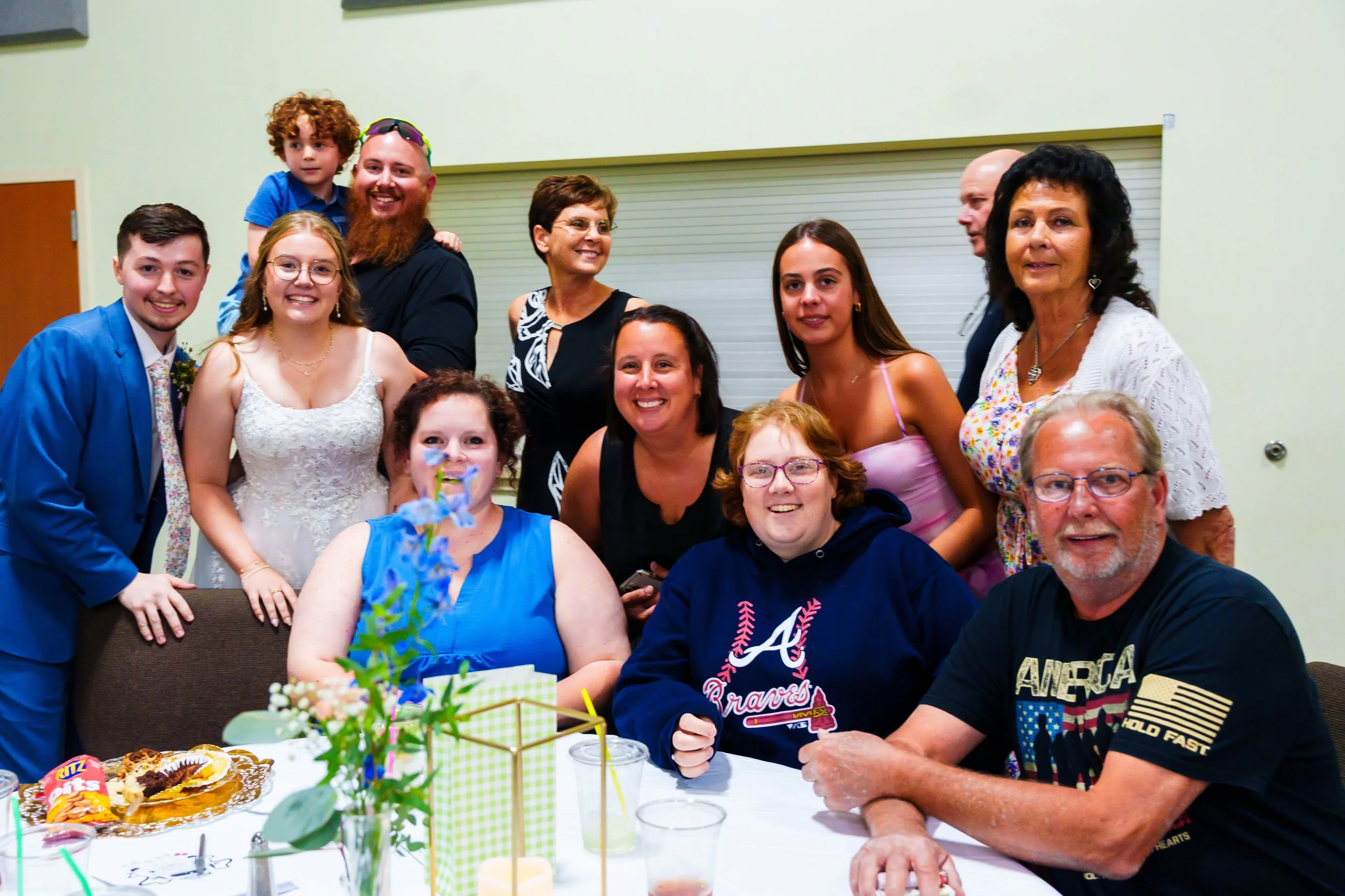 Group of people celebrating around a table with birthday cake and snacks, smiling and enjoying the moment.