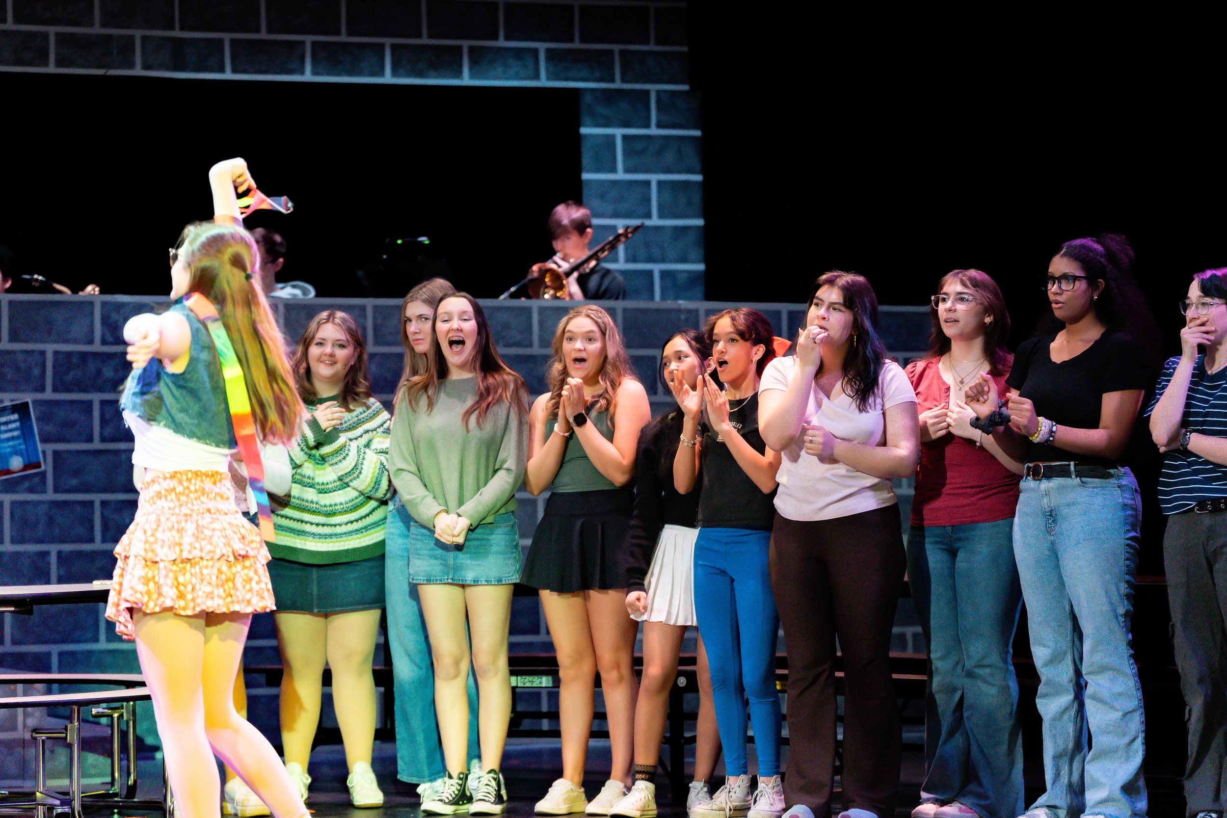 A group of young women watching a performer on stage, with some showing surprise and excitement.