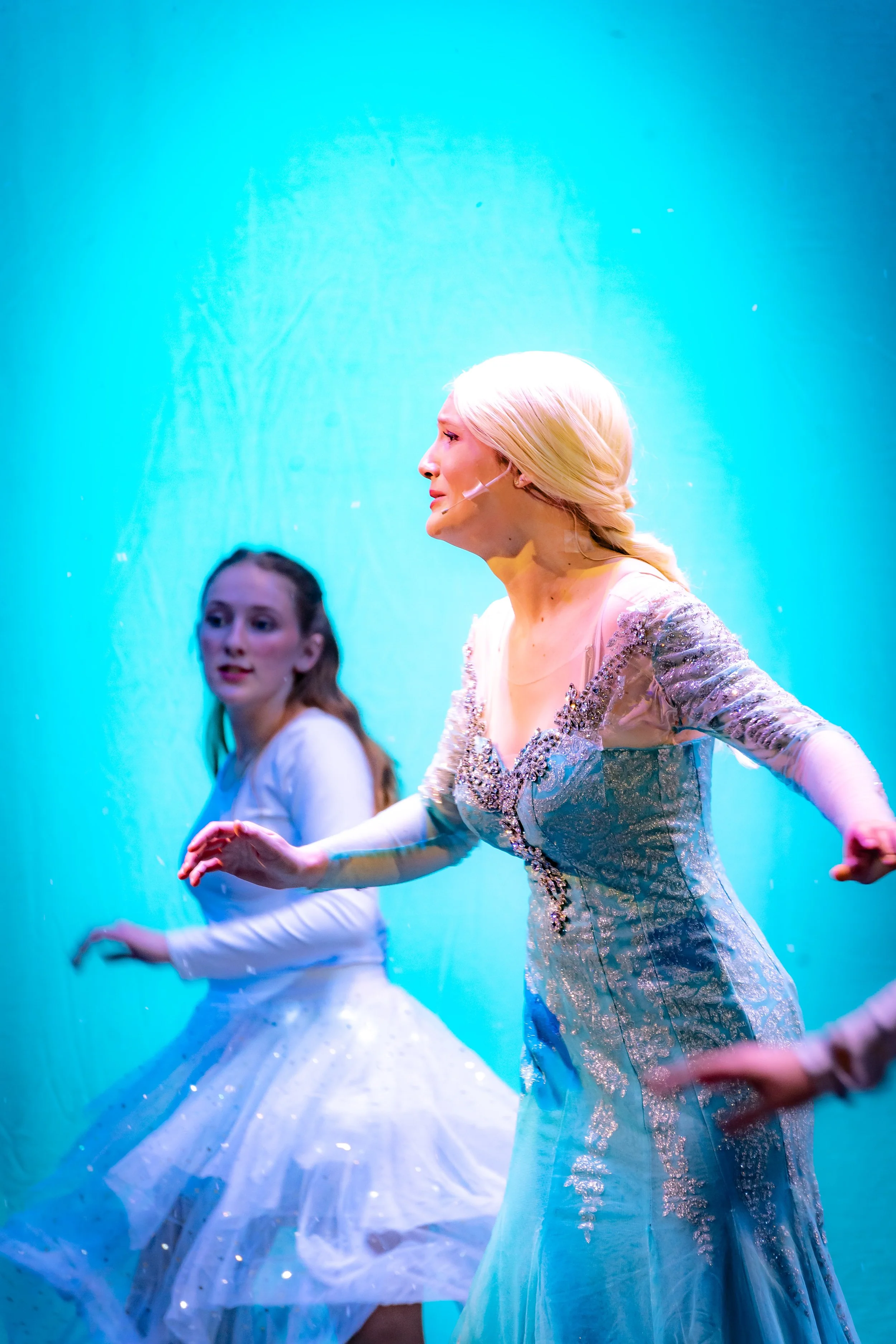 Two women performing ballet on stage, dressed in ornate costumes with a glowing blue background.