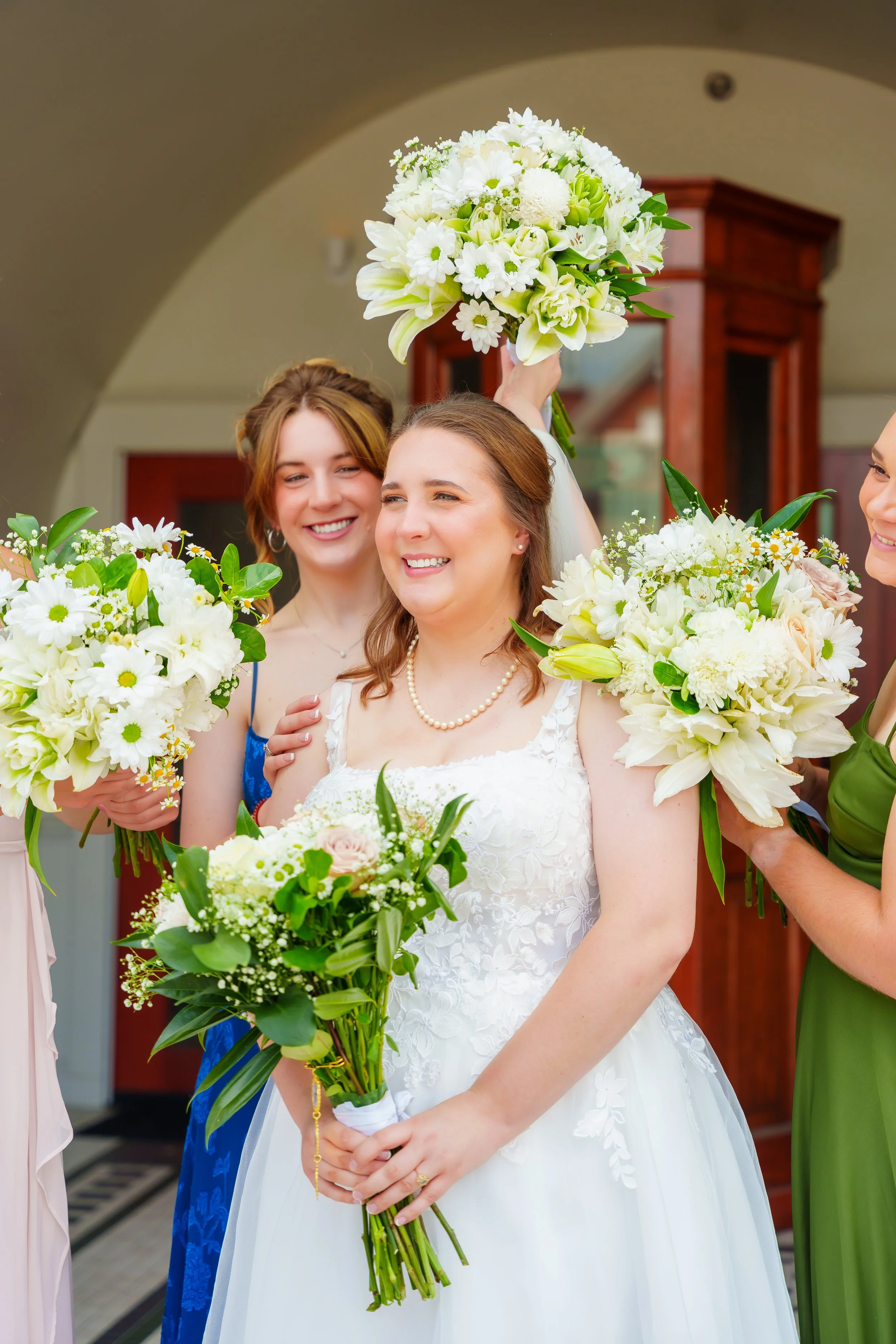 A bride holding a bouquet of white flowers, surrounded by women with similar bouquets, at a wedding ceremony.