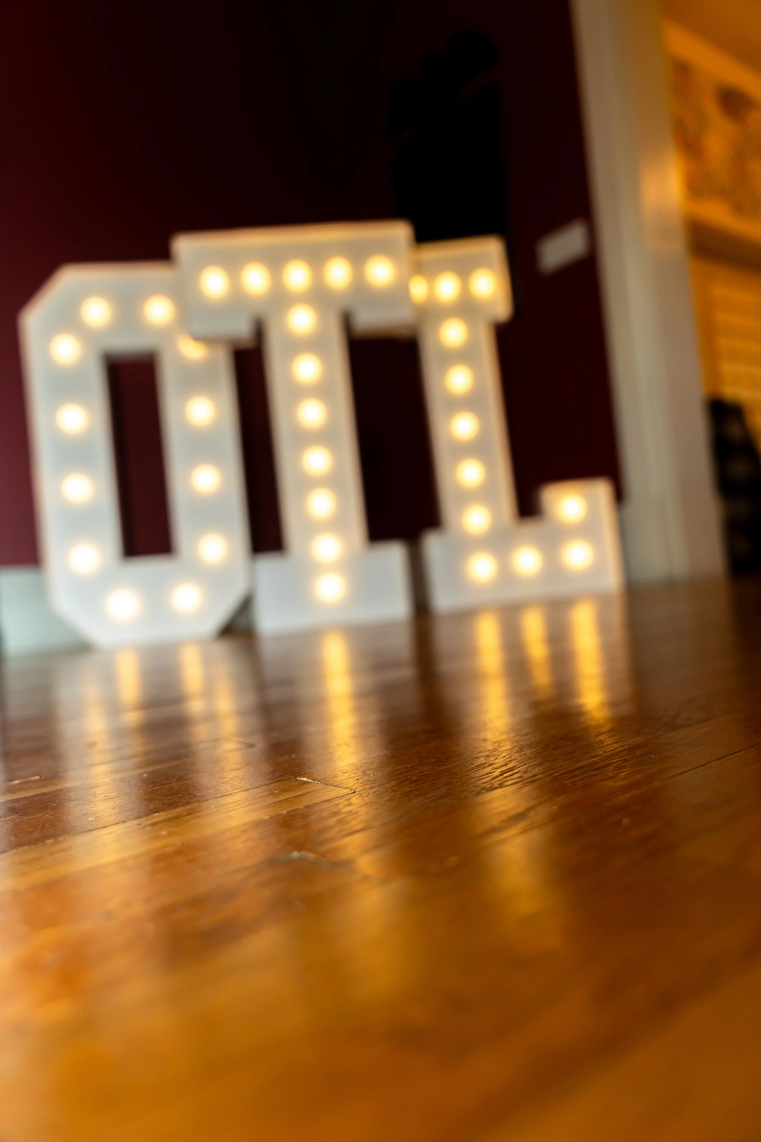 A decorative lighted marquee letter L on a wooden floor against a dark background.