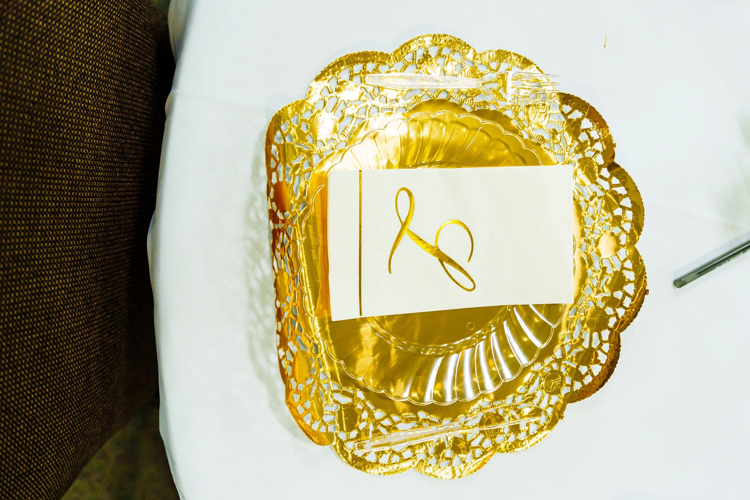 Gold-colored decorative plate with intricate lace-like edges, featuring a white card with a gold diagram on it, set on a white surface.