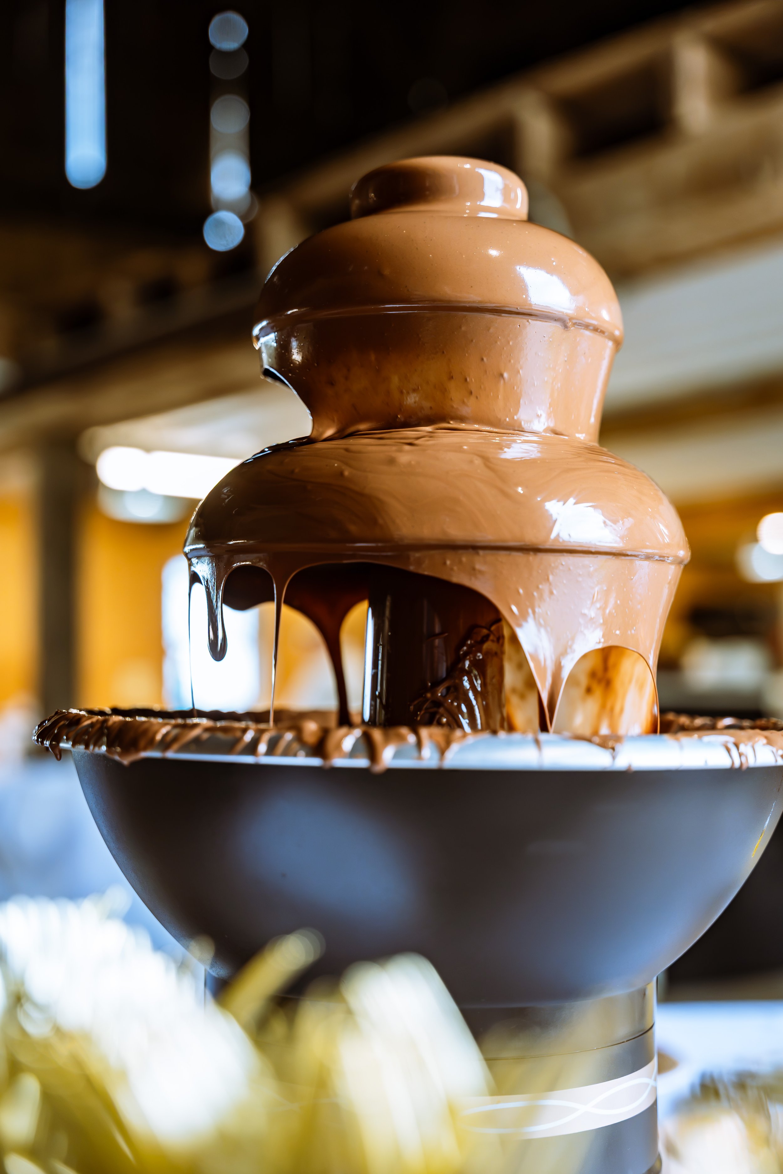 Close-up of a chocolate fountain with melted chocolate cascading down tiers, set in a cafe or restaurant setting.