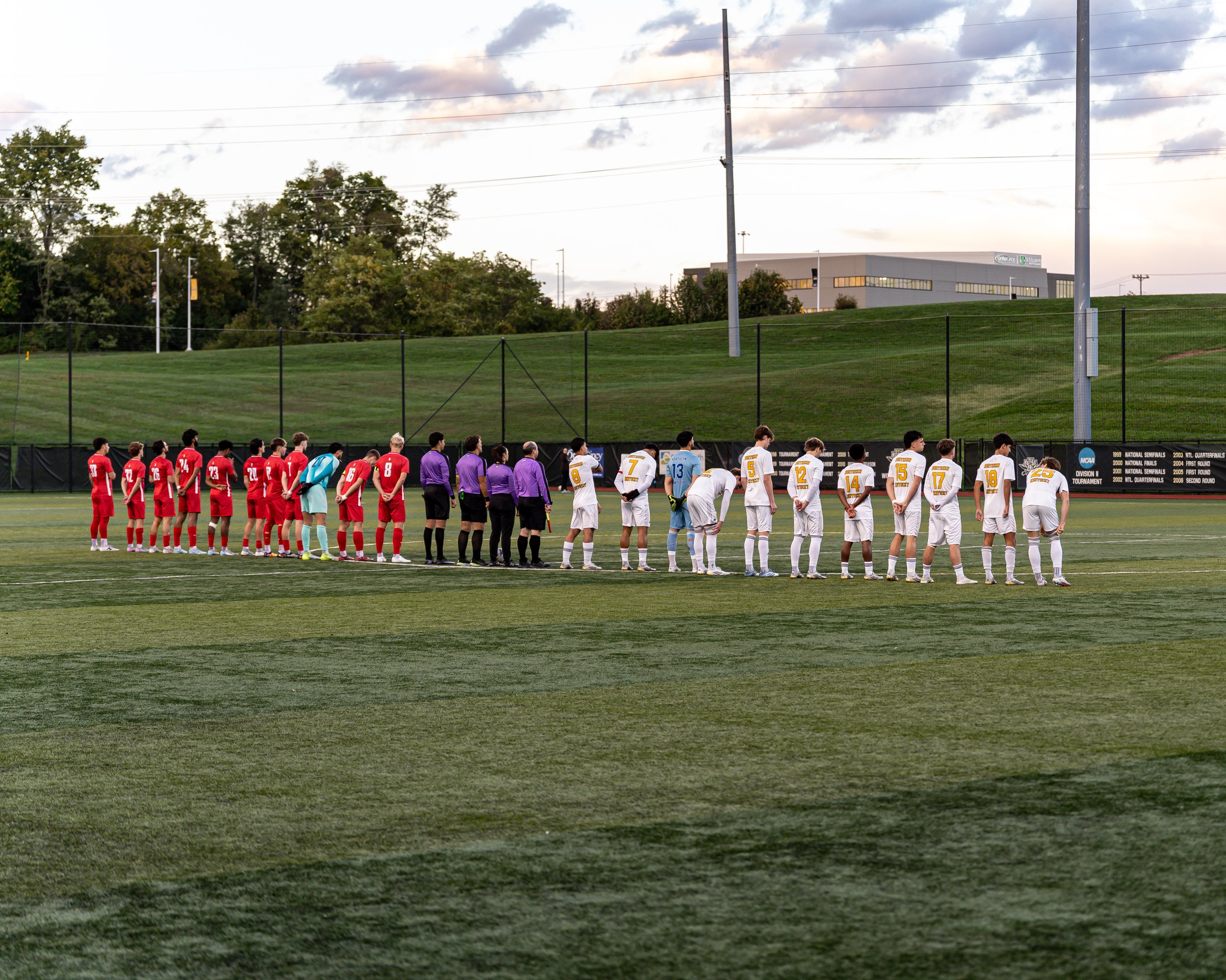 Soccer players and referees standing in line on the field before a match at sunset.