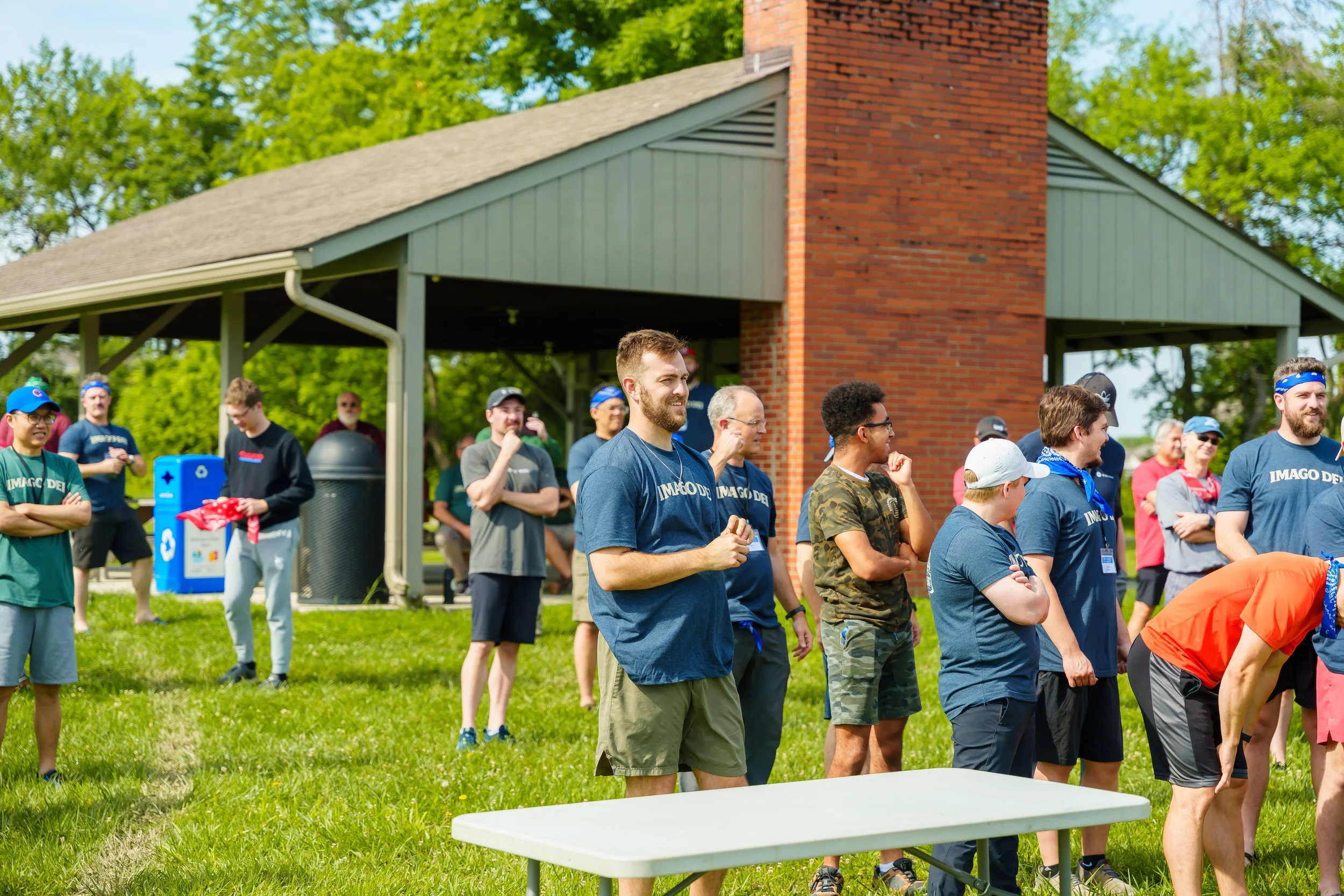 A group of people gathered outdoors on a grassy area near a brick building, participating in an event or activity on a sunny day.