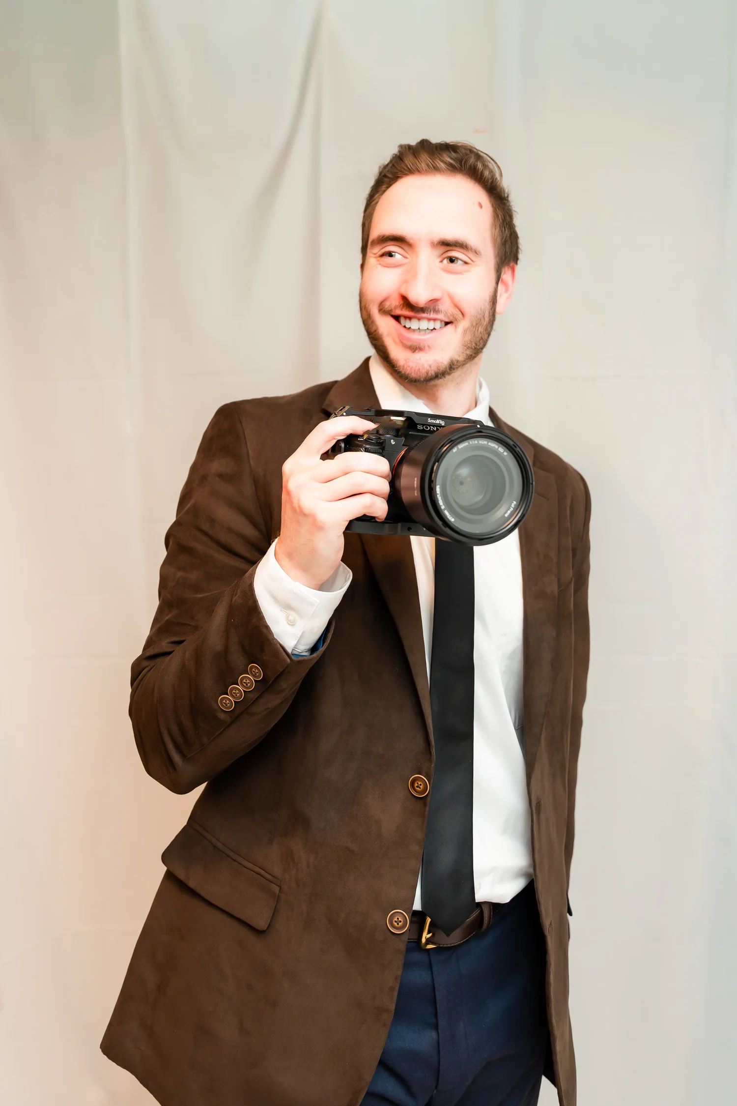 Seth smiling in a red sweatshirt, holding a camera at a sporting event