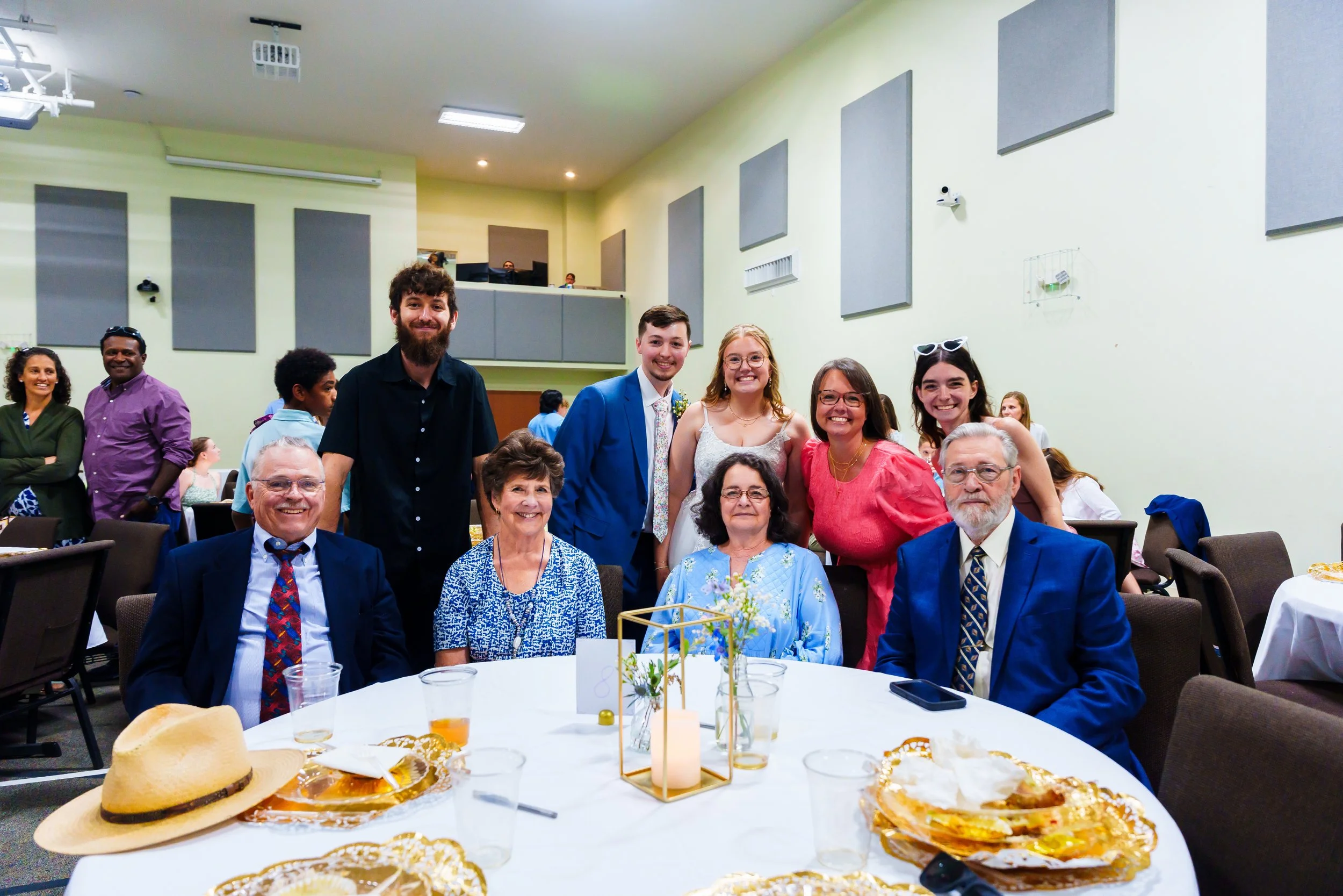 Group of people celebrating at a banquet, with decorations, food, and drinks on the table, in an indoor hall.