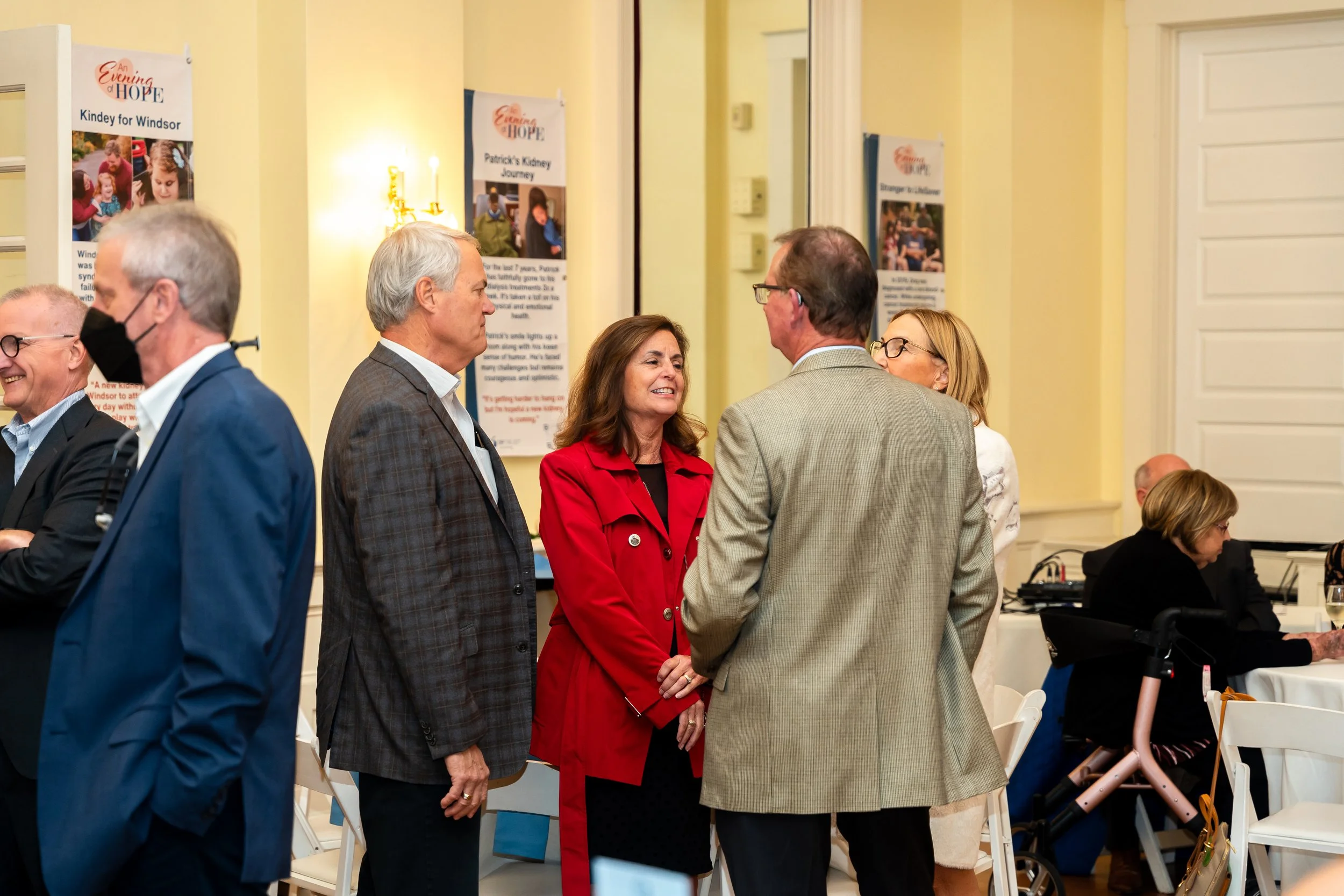 People socializing indoors at a charity or community event, with posters in the background.