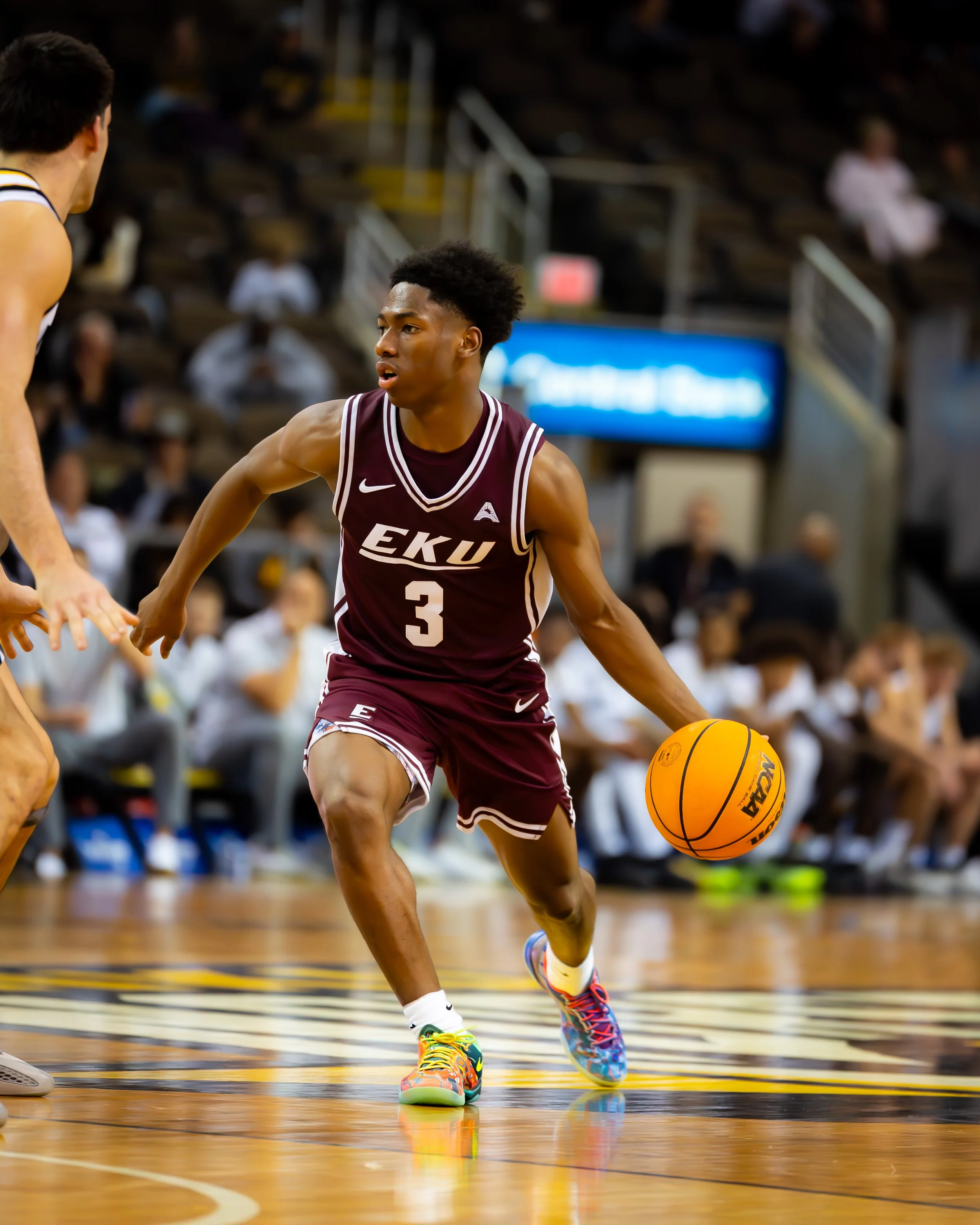 A basketball player from EKU, wearing jersey number 3, dribbling an orange basketball on the court.