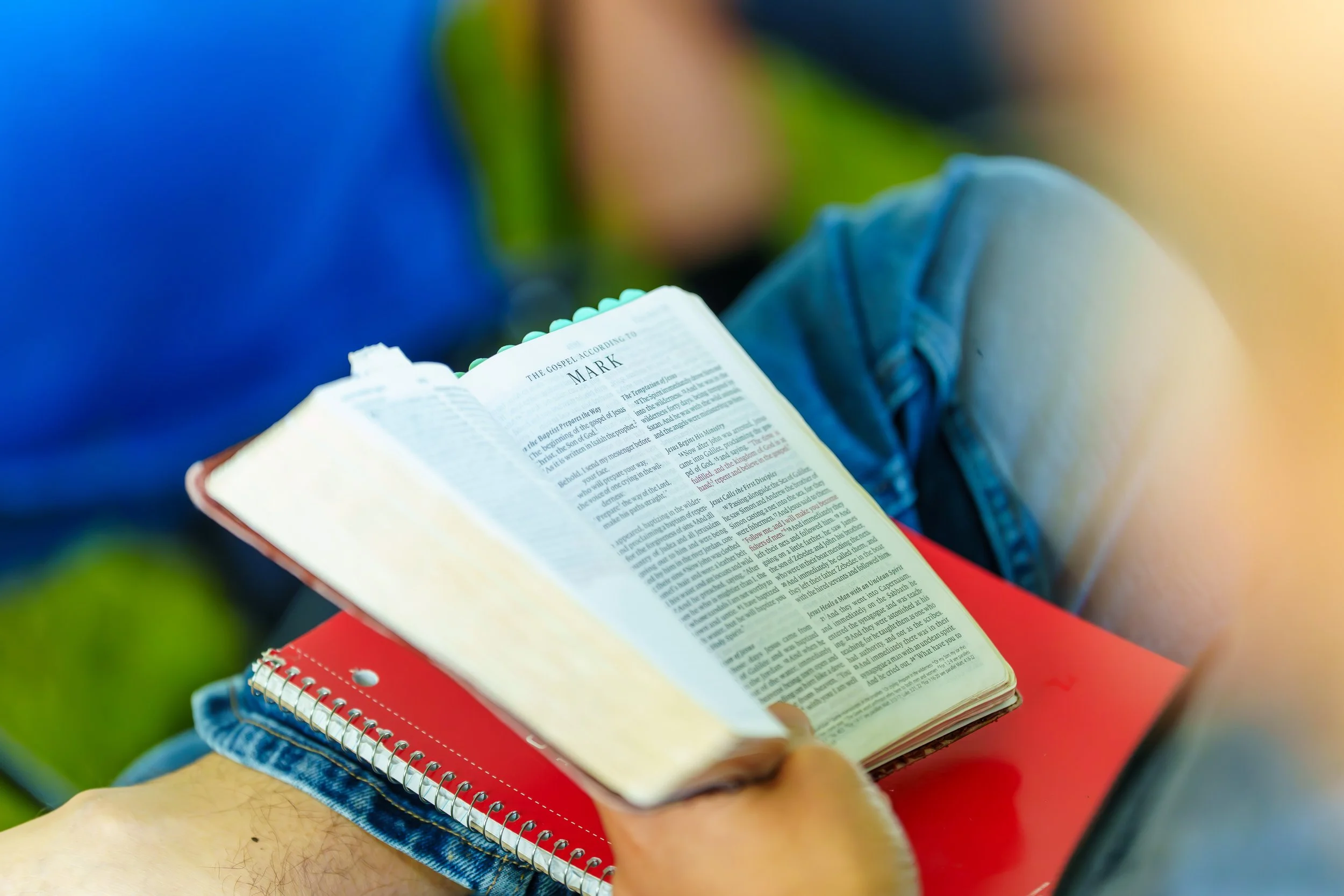 Person sitting outdoors reading a Bible, focusing on the open page with the word 'Mark' visible at the top.
