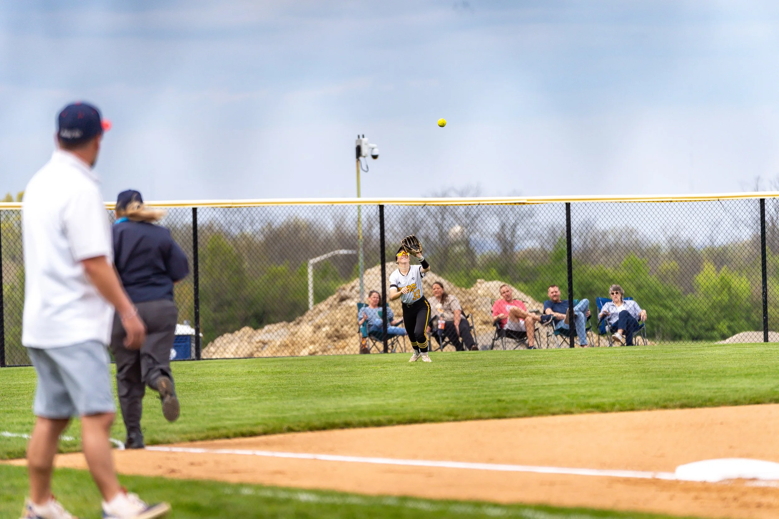 A softball game in progress with a player catching a ball and spectators watching from the stands.