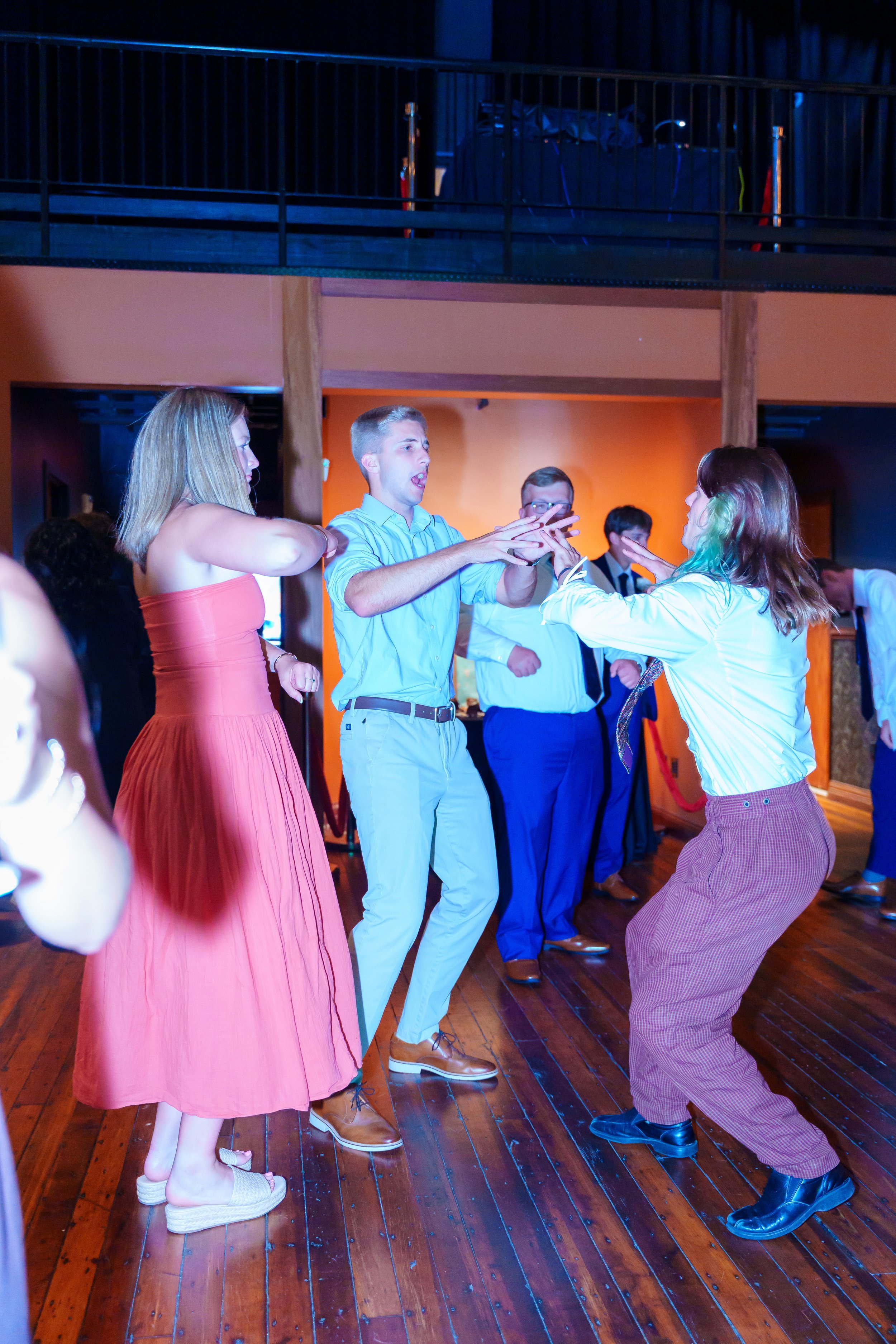 People dancing and socializing at a party or event in a room with wooden floors and colorful walls.