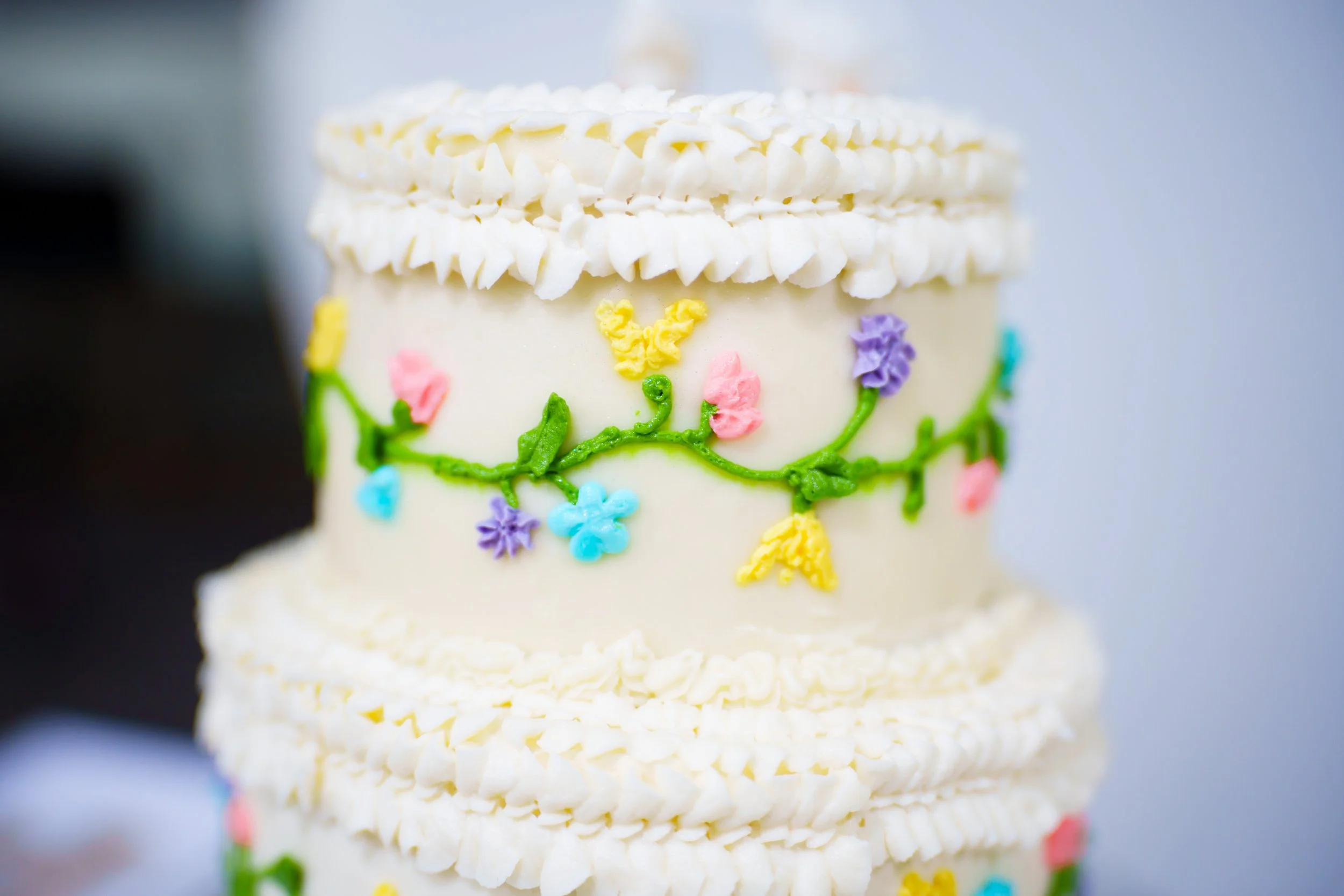 Close-up of a decorated birthday cake with white and colorful floral piping and icing.