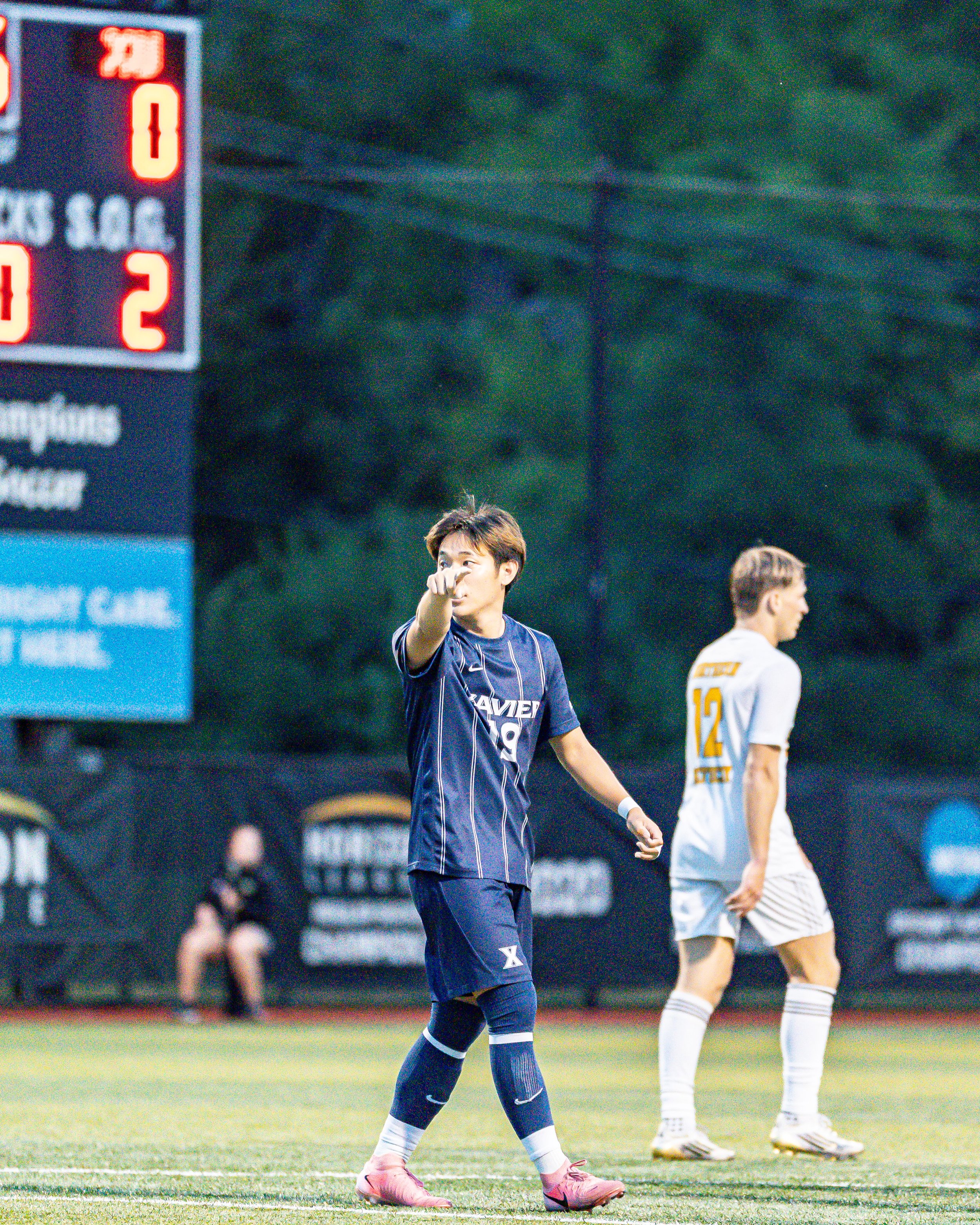 Soccer player on the field pointing with the scoreboard in the background.