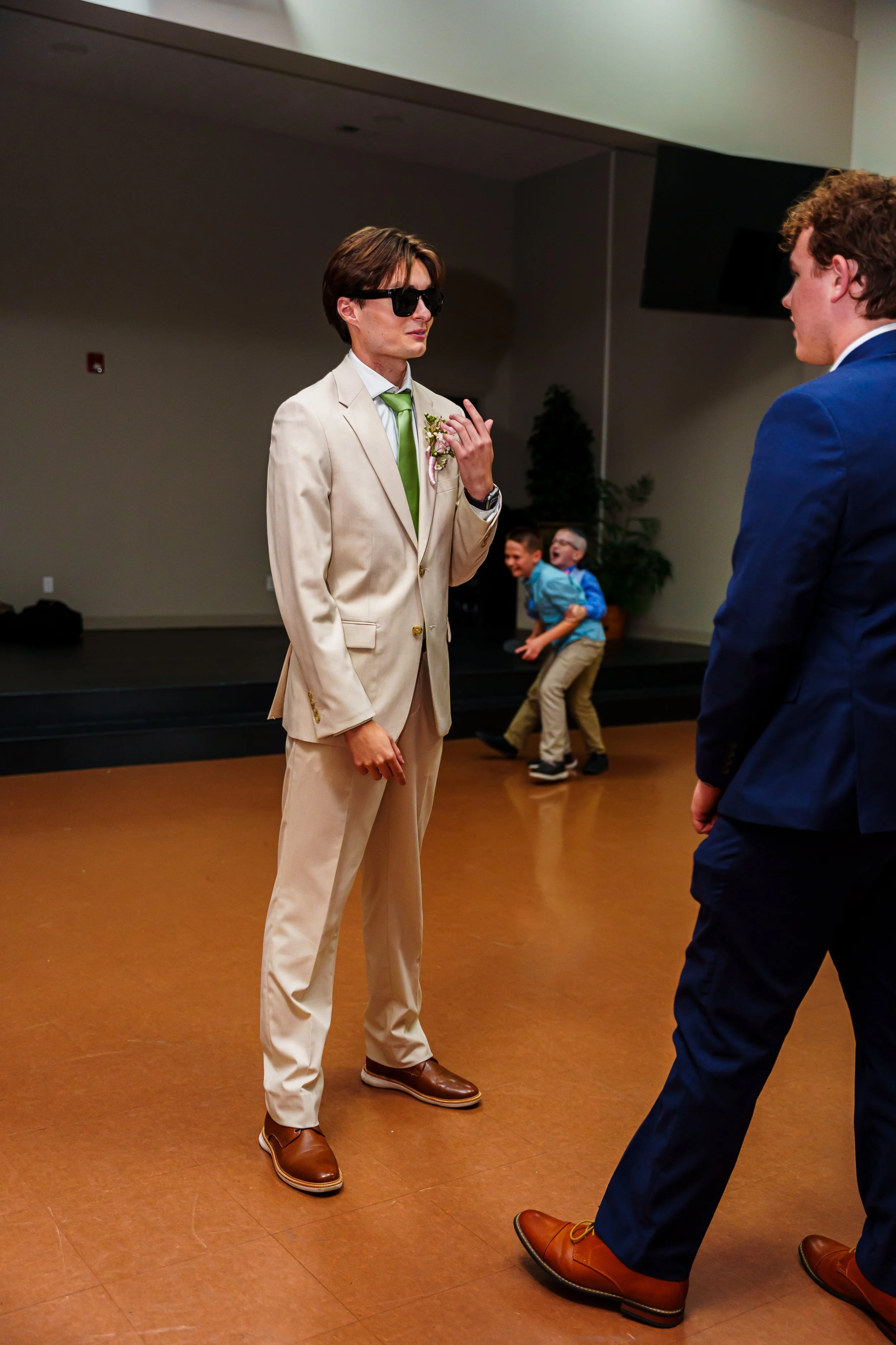 Two men in suits dancing at a social event, with three children playing and laughing in the background.