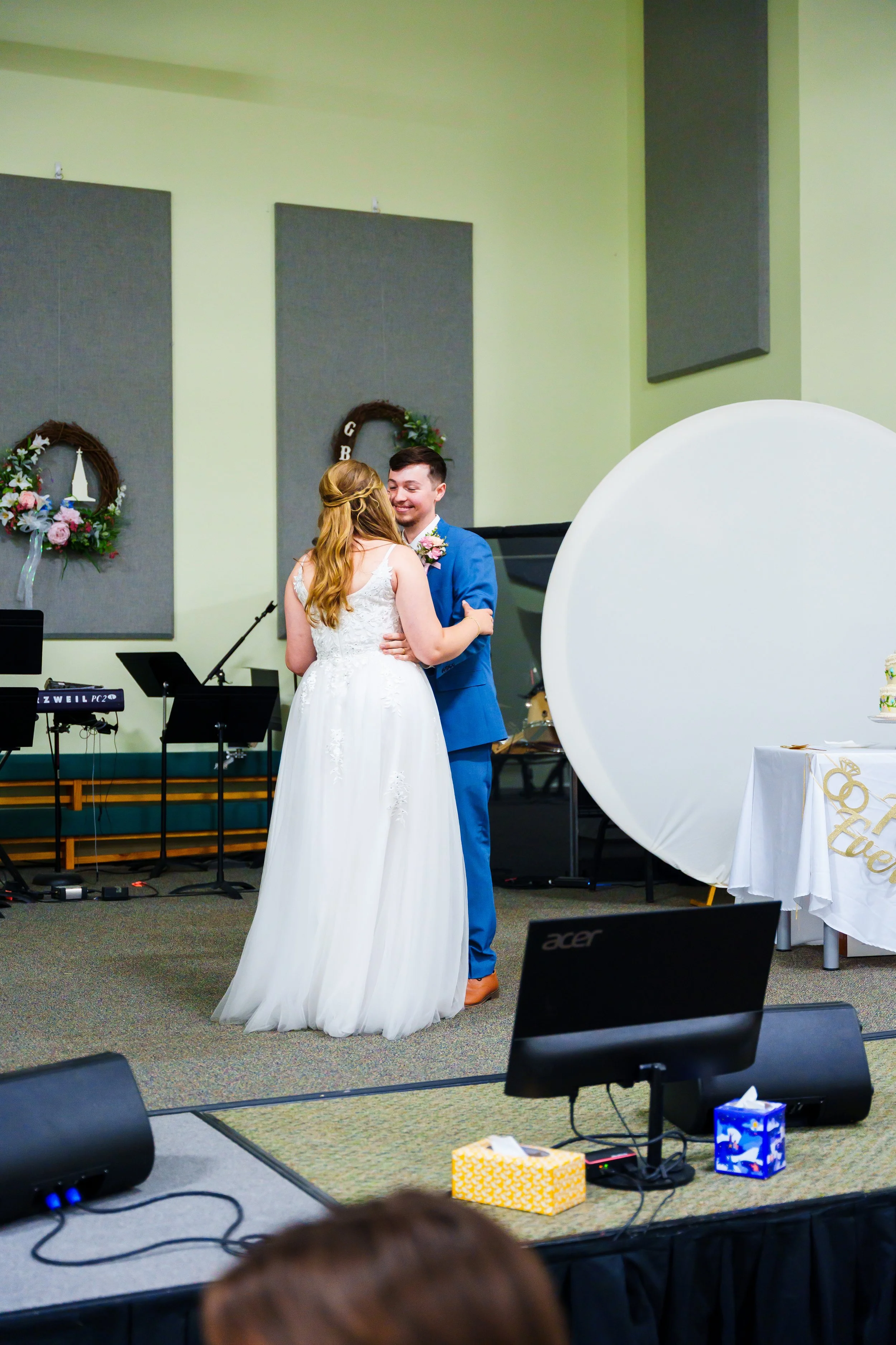 A bride and groom dancing at their wedding reception in a decorated hall with musical instruments and gifts visible.