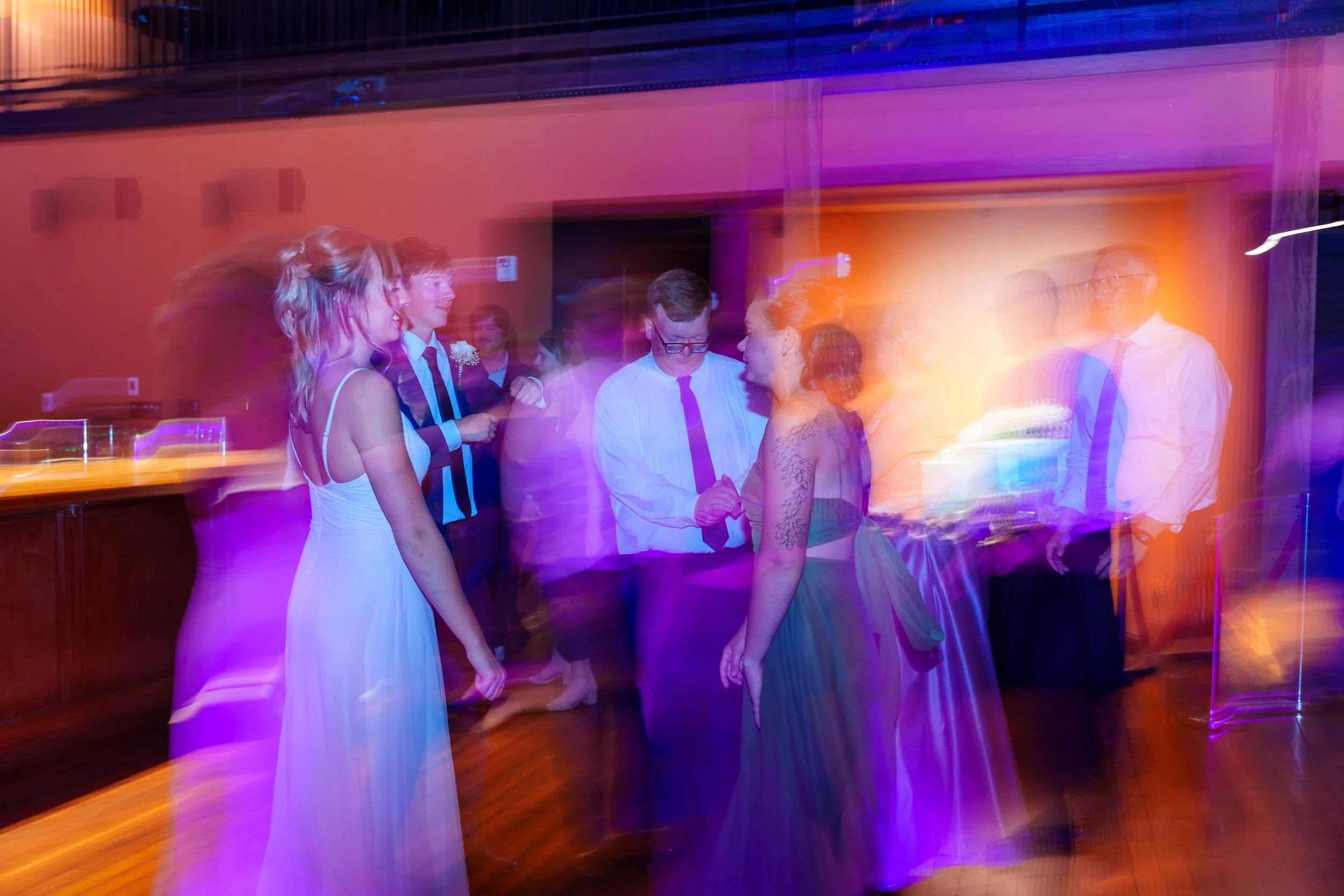 A group of people dancing at a party with colorful lighting.