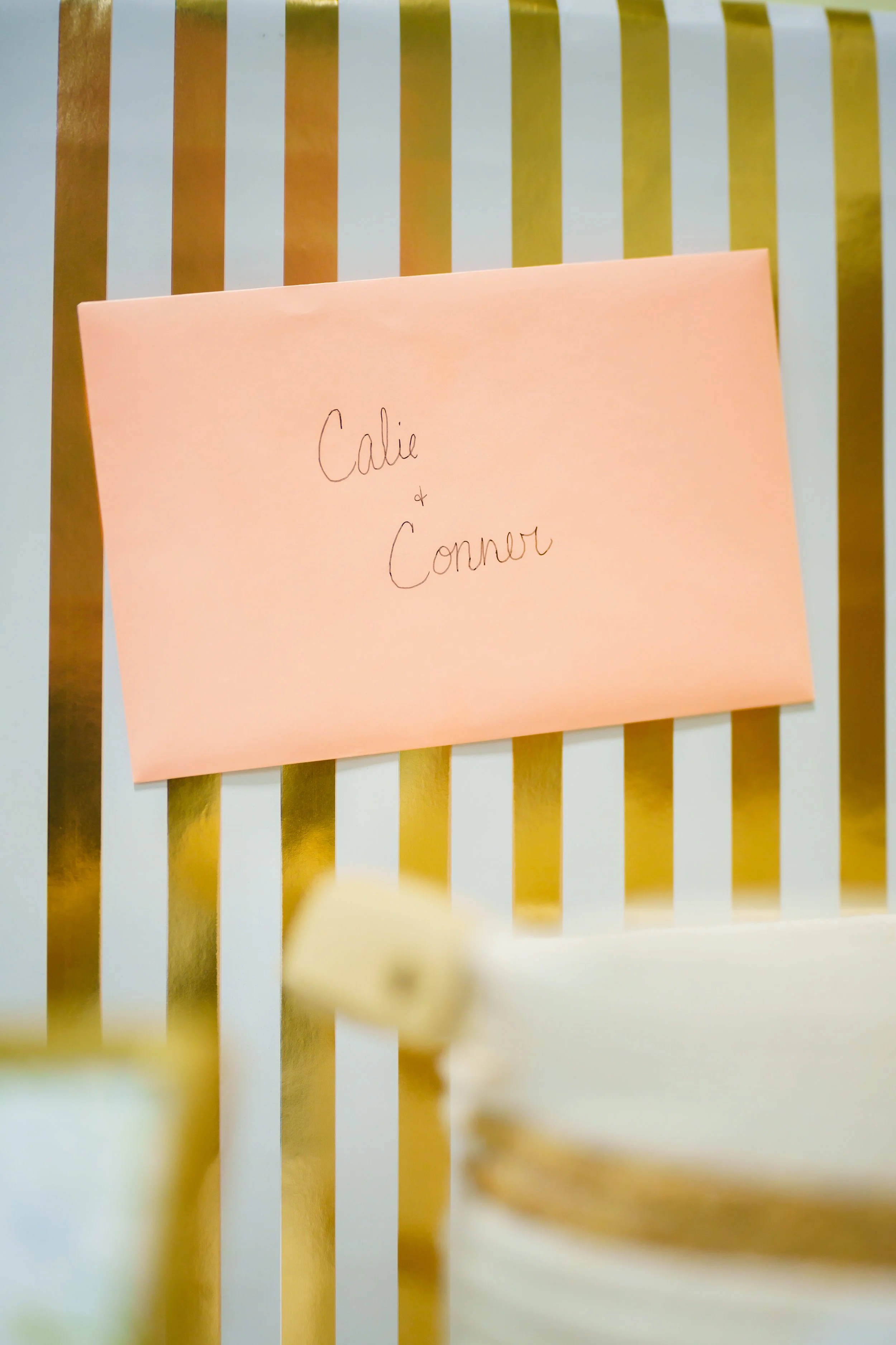 A pink sticky note with the handwritten words 'Calie & Connor' is attached to a gold and white striped surface.