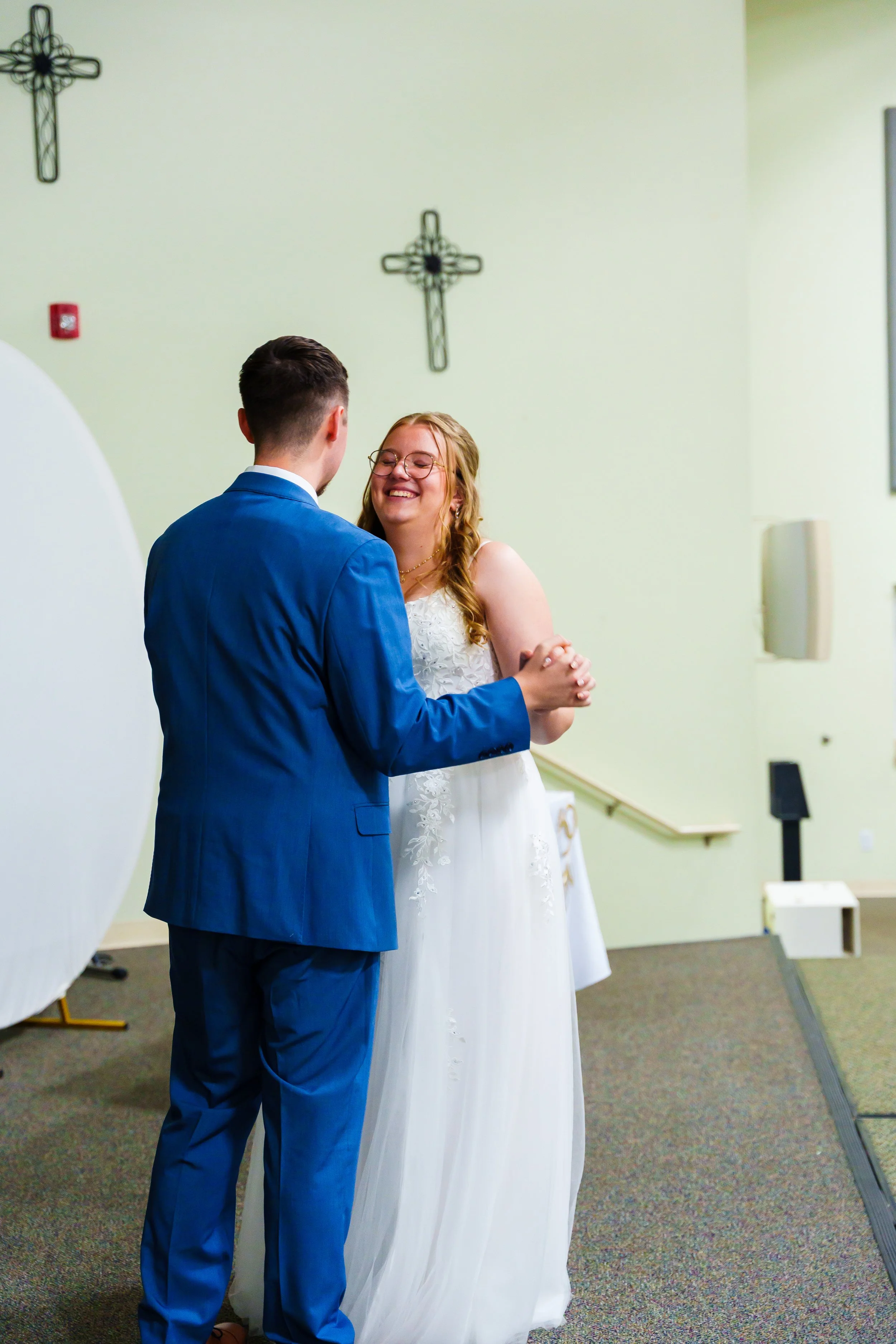A couple wedding dancing in a venue with white walls and religious crosses on the wall.