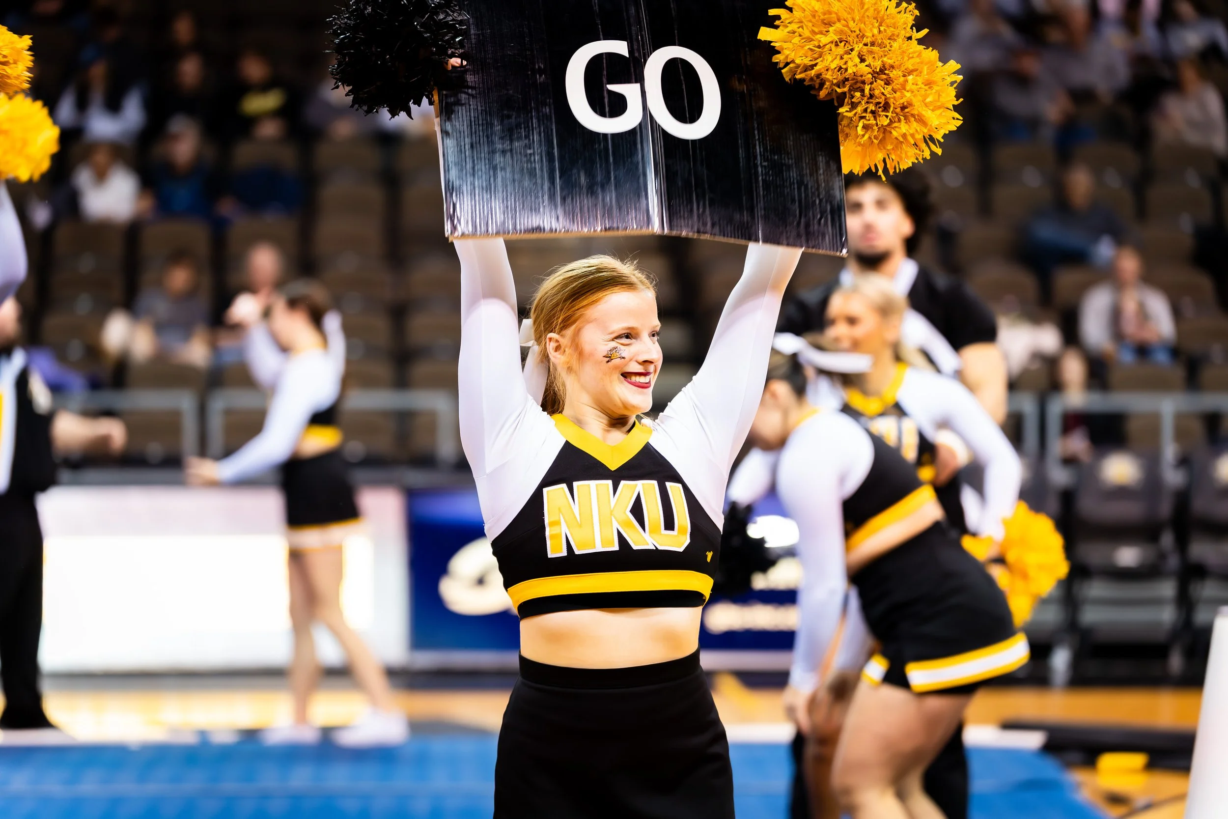 A cheerleader from NKU holding a sign that says 'GO' at a sports event.