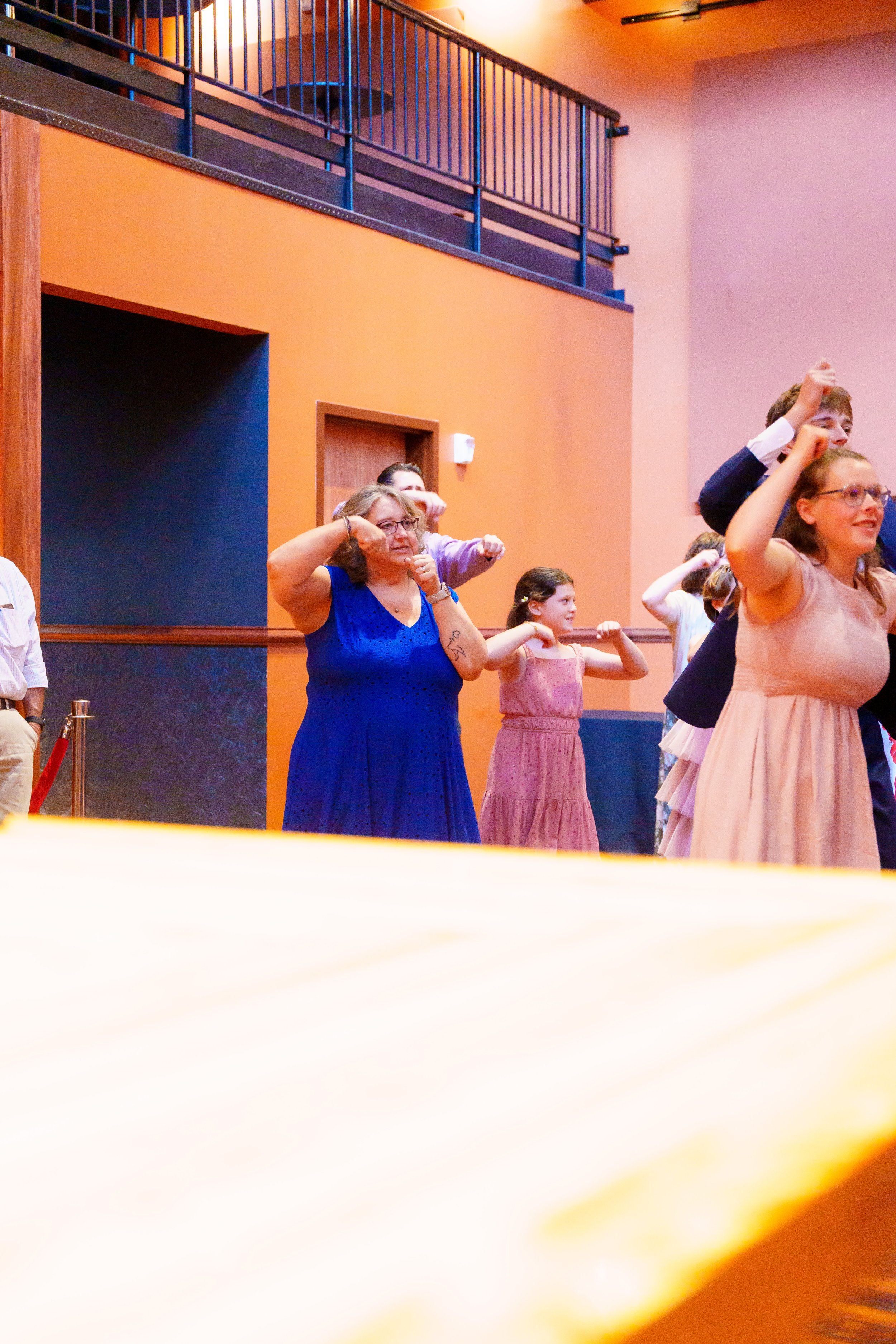 Group of people, including children and adults, standing in a room with warm-colored walls, participating in an activity with their fists raised in a salute or gesture of empowerment.